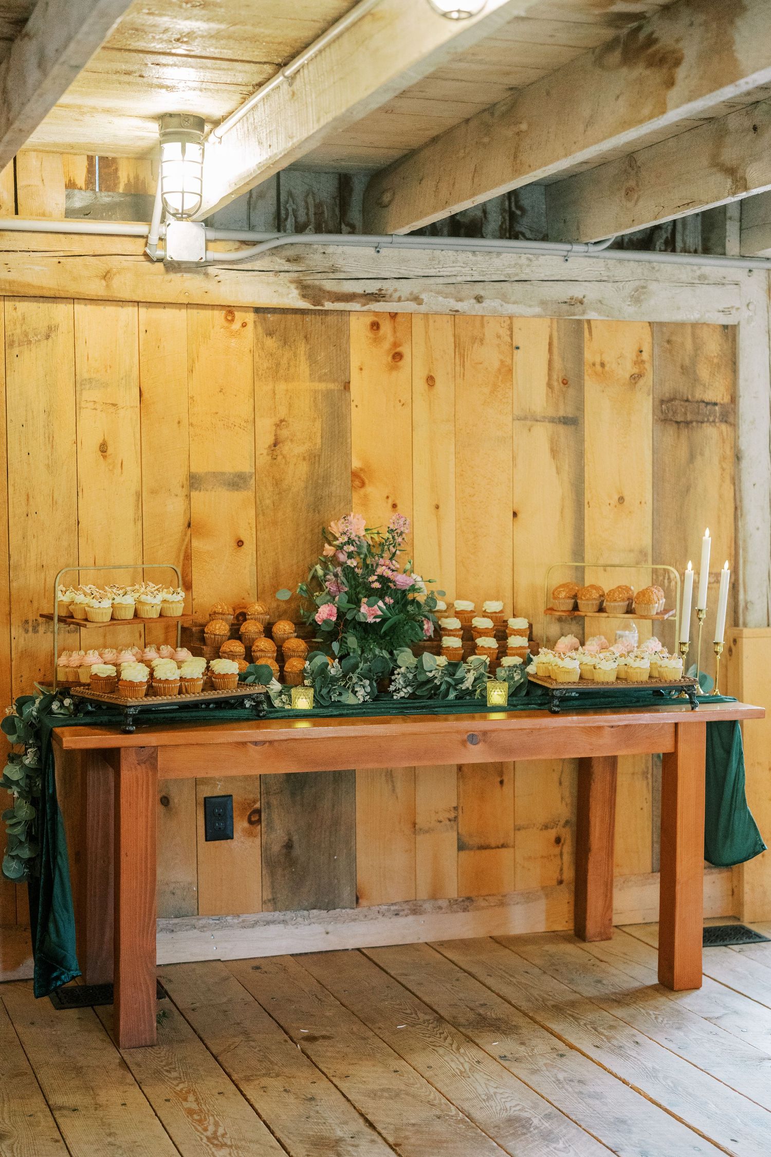 Rustic wooden benches with mason jar centerpieces and greenery garlands line the wall of a barn-style venue.
