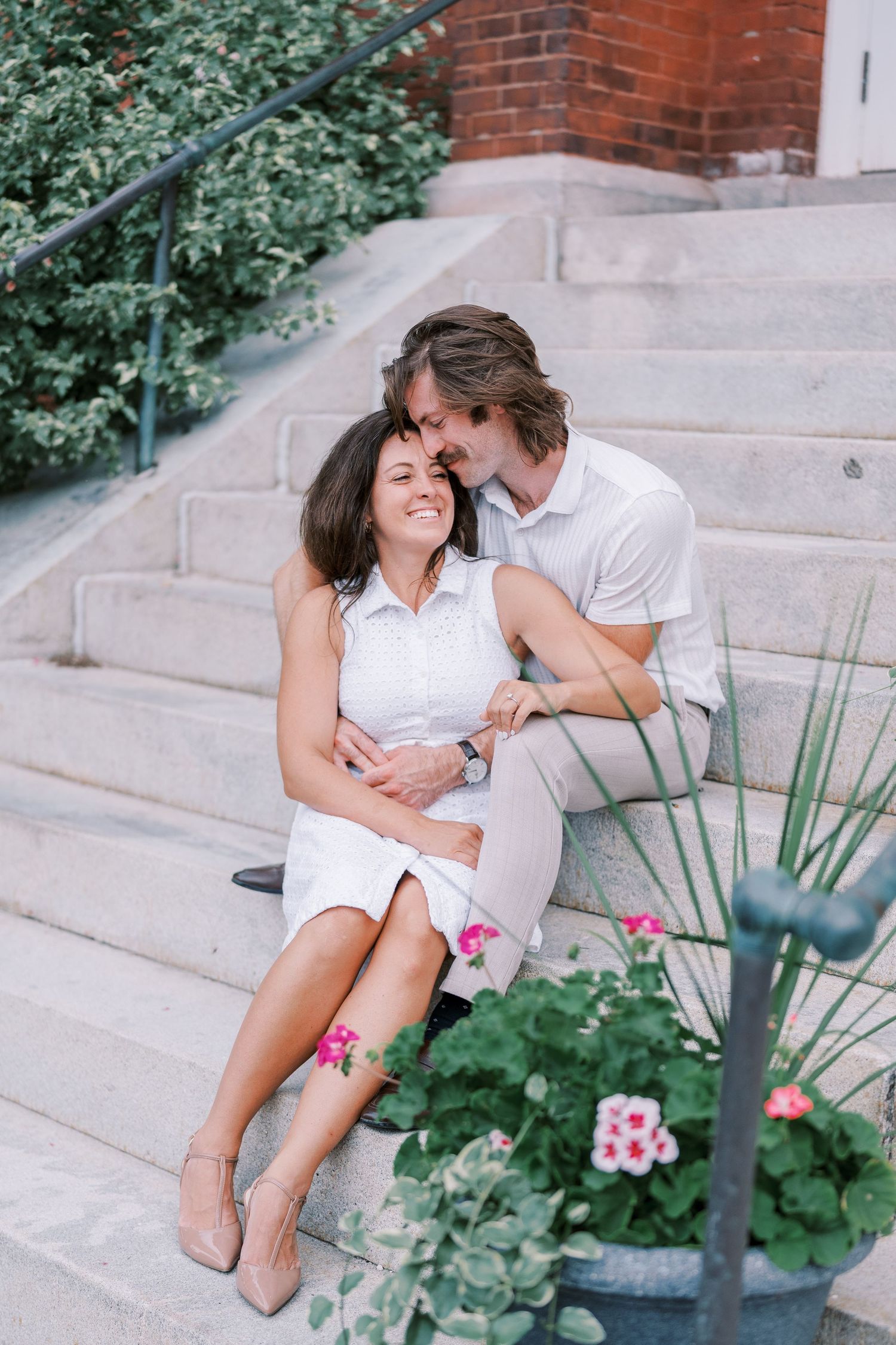 A romantic moment shared on concrete steps with pink flowers and greenery.