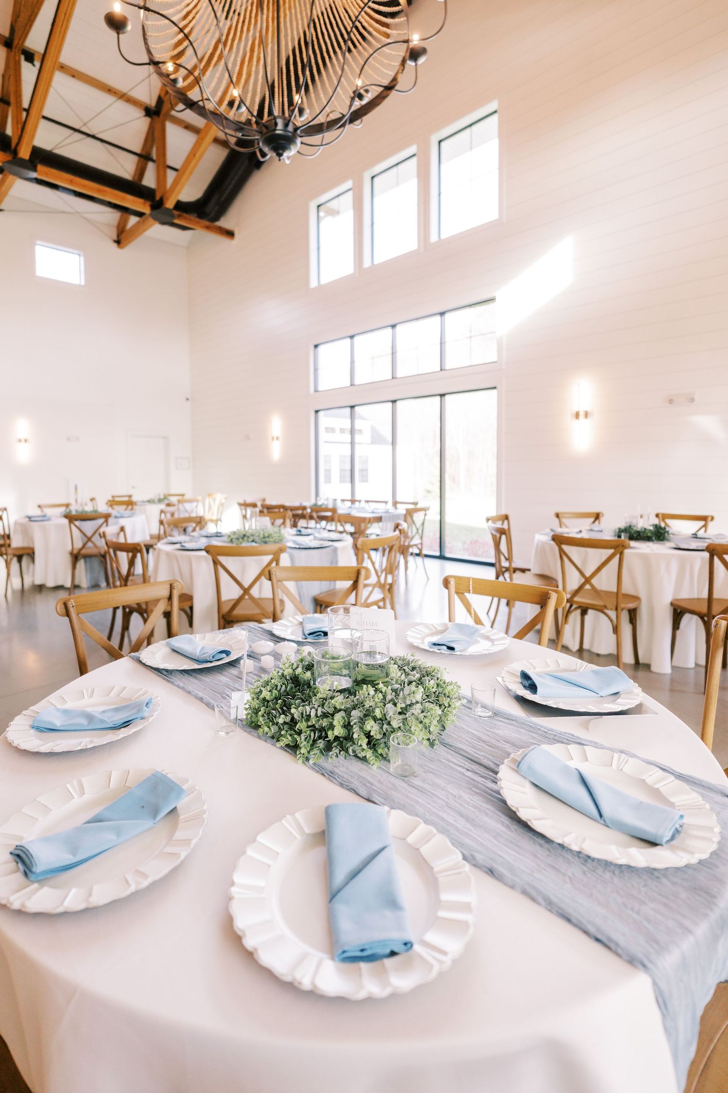White and blue table settings with rustic wooden chairs in a bright modern venue with high ceilings and natural light.