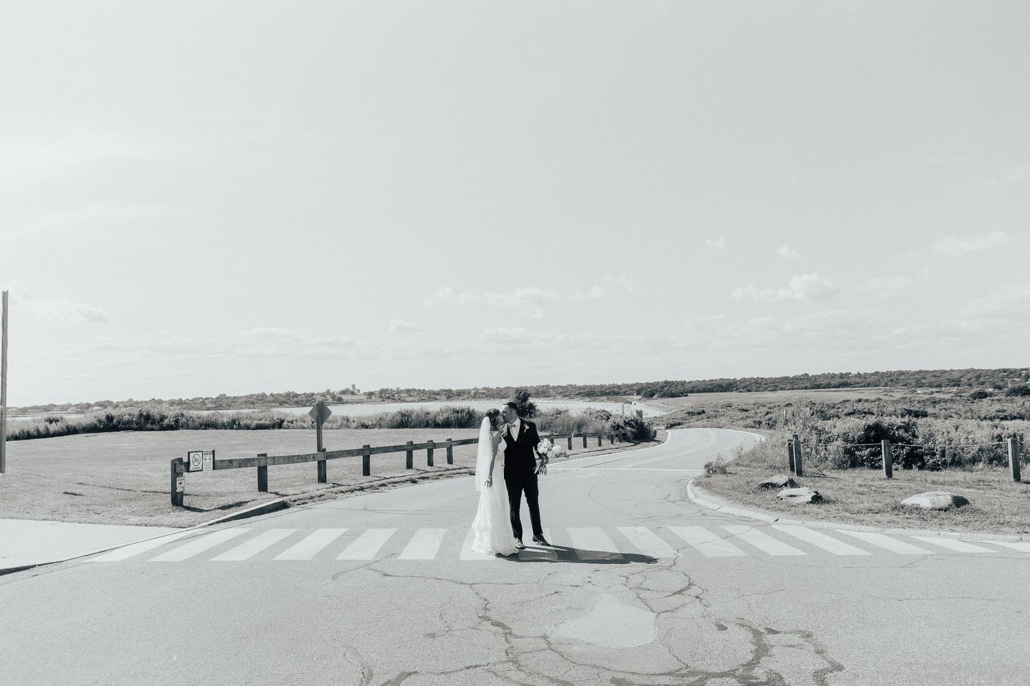 A black and white panoramic photo shows a person walking along a snowy winter road through a vast rural landscape.