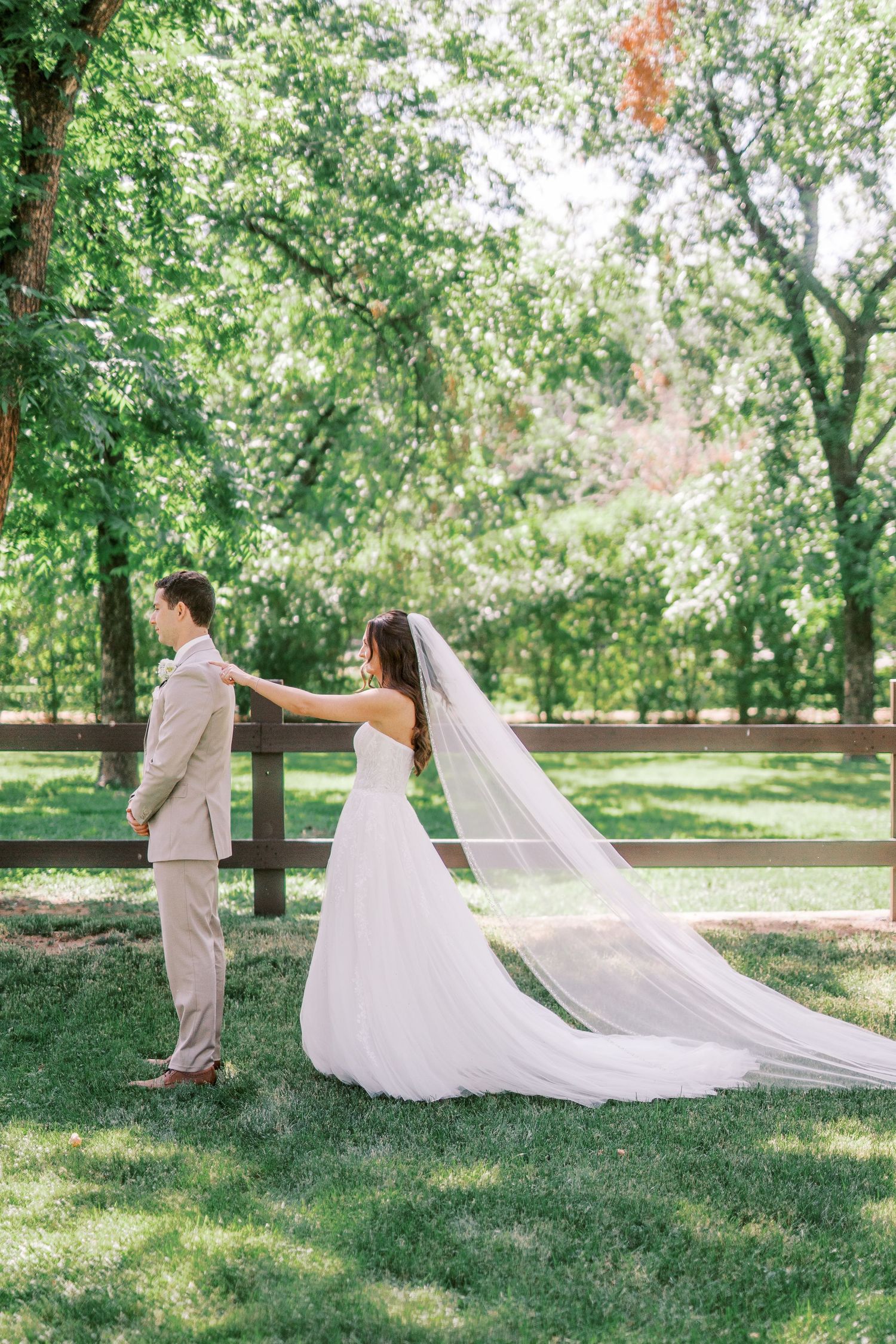 A couple in formalwear walking apart on a sunny day in a park setting with trees and green grass around them.