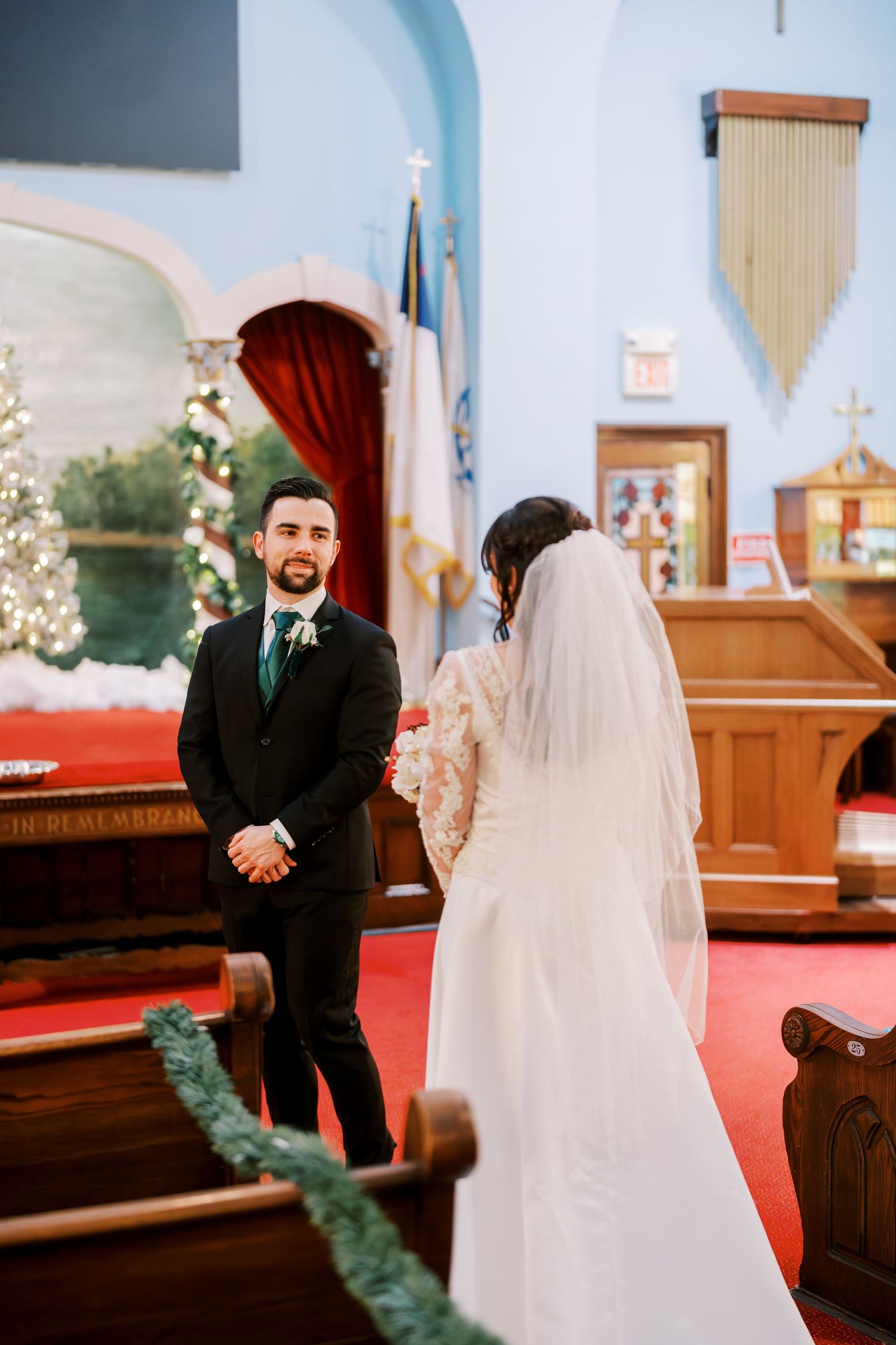A wedding ceremony takes place inside a church with red carpet and holiday decorations visible.