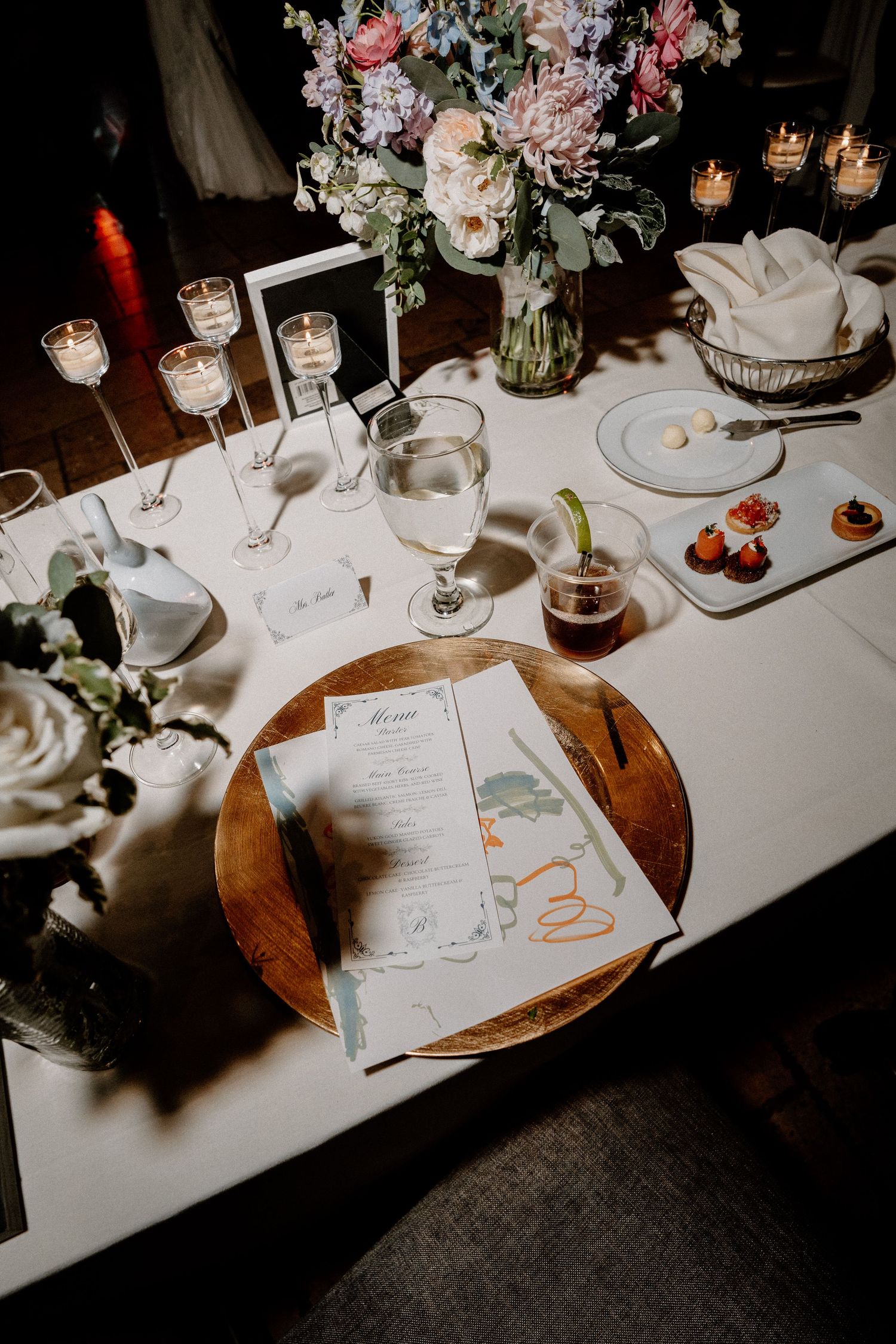 Elegant wedding reception table settings with white linens, floral centerpieces, and menu cards in romantic candlelight.