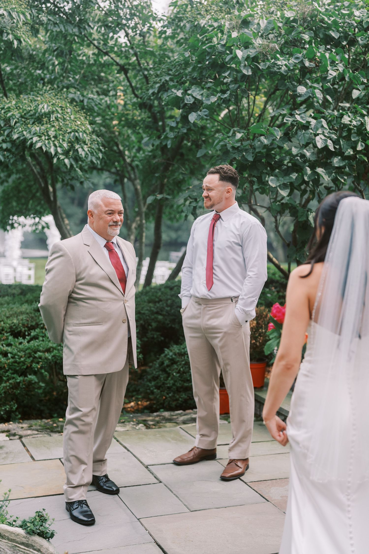 Wedding party members in light suits gather in a garden setting with fountain.