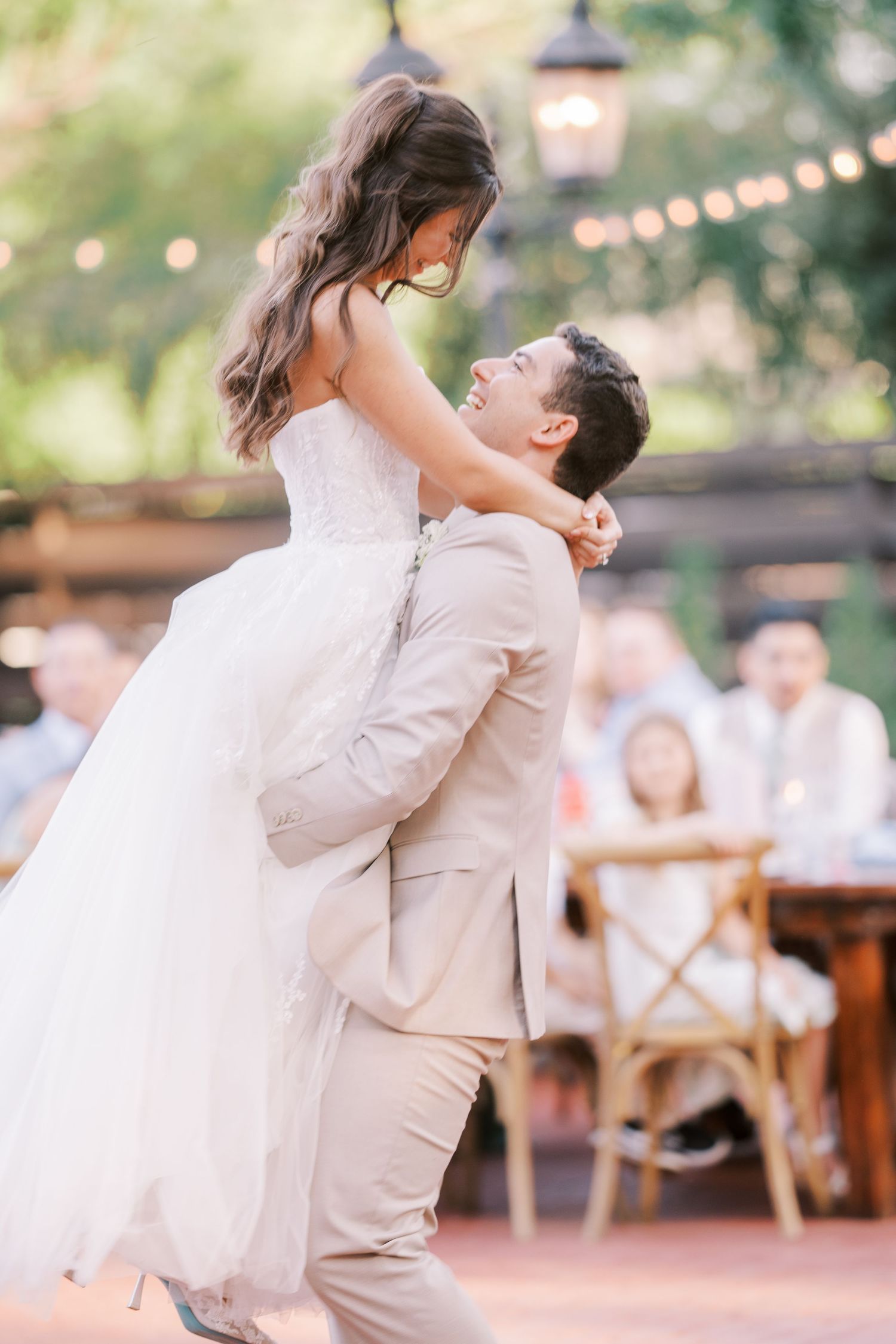 A couple shares a joyful dance moment at an outdoor wedding reception with string lights visible in the background.