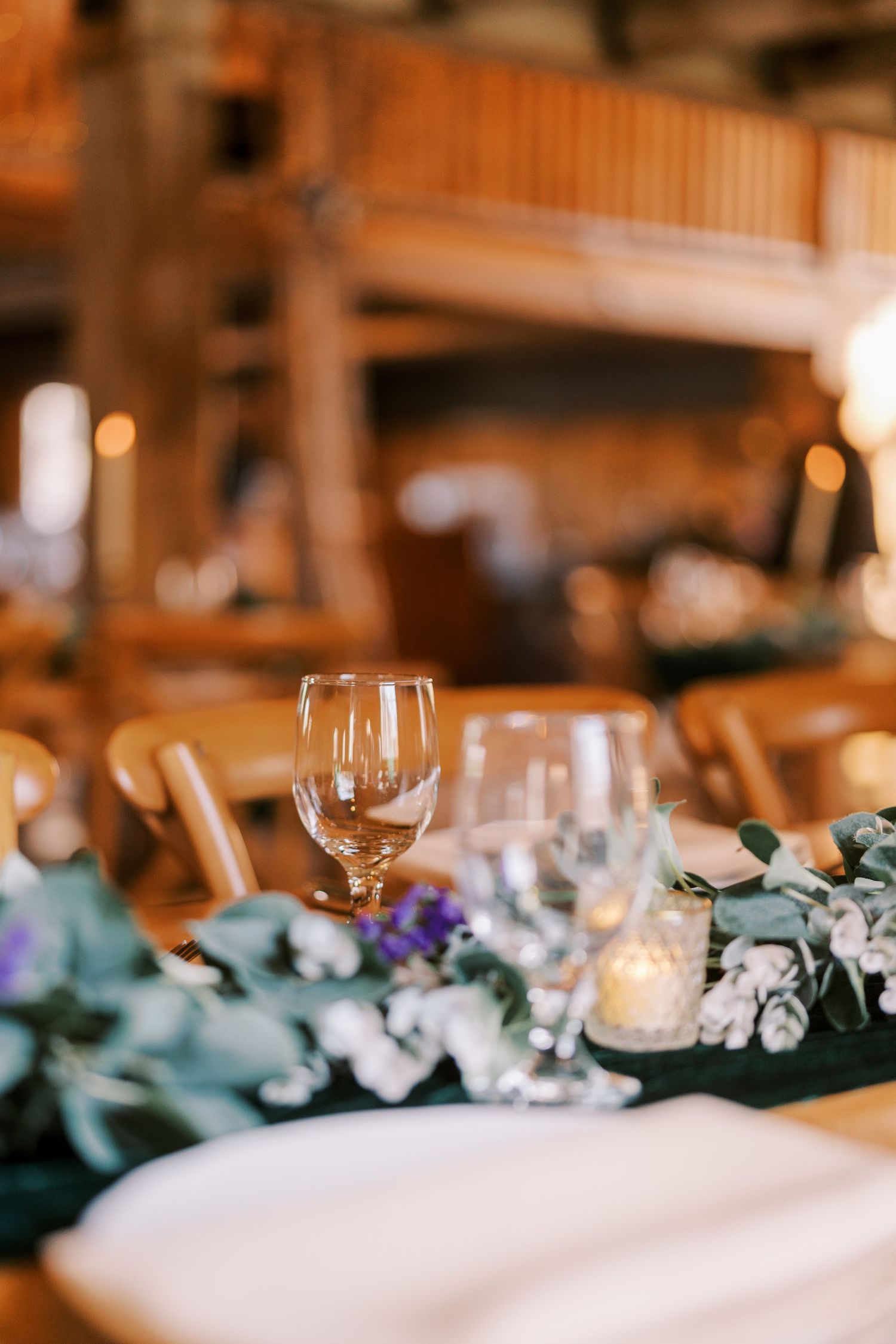 Elegant wedding reception table setting with wine glasses and floral decorations in warm ambient lighting.