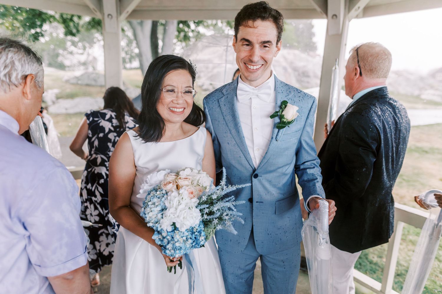 Wedding party gathering under a white gazebo during outdoor ceremony.