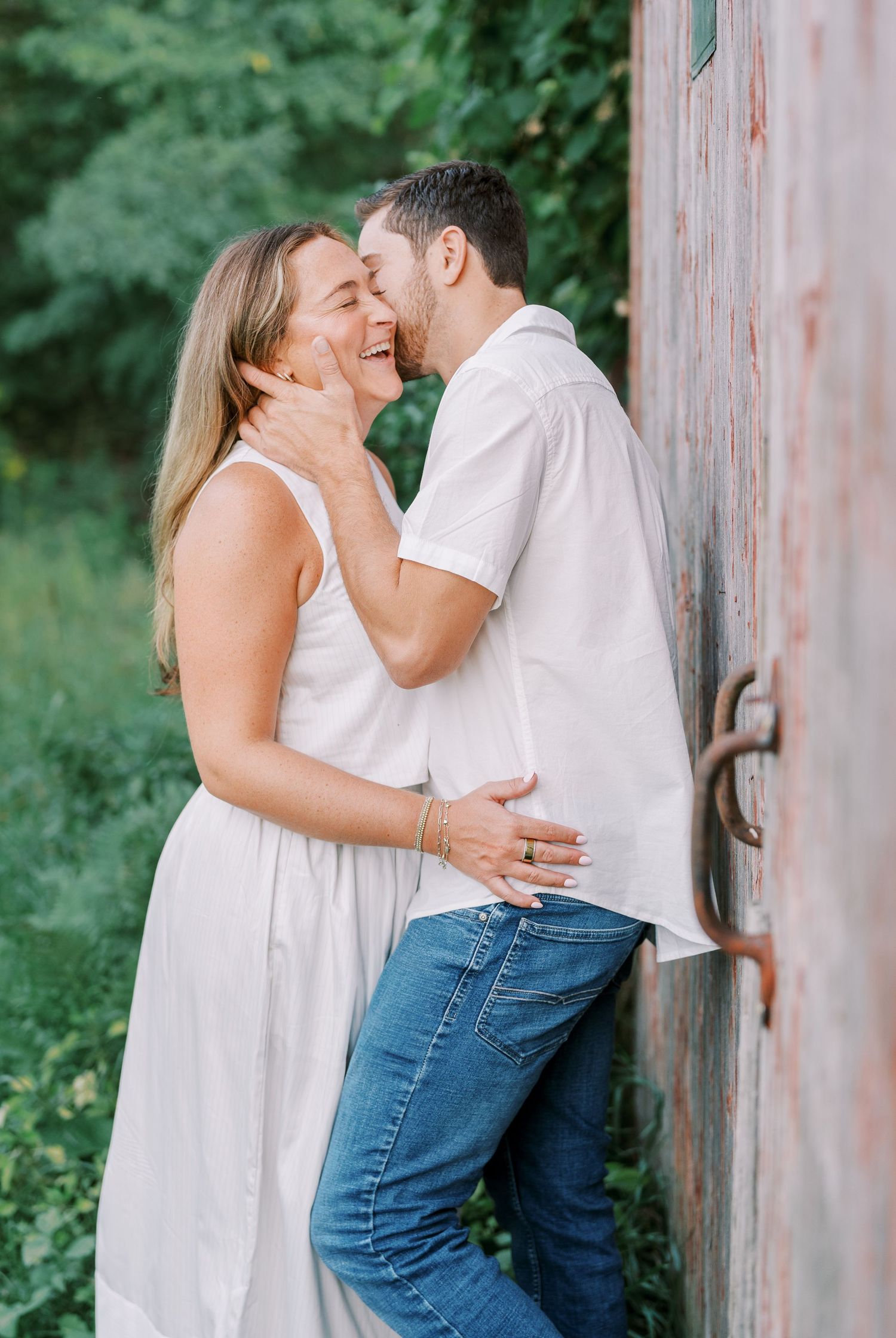 A romantic moment shared against a rustic barn wall in casual summer attire.