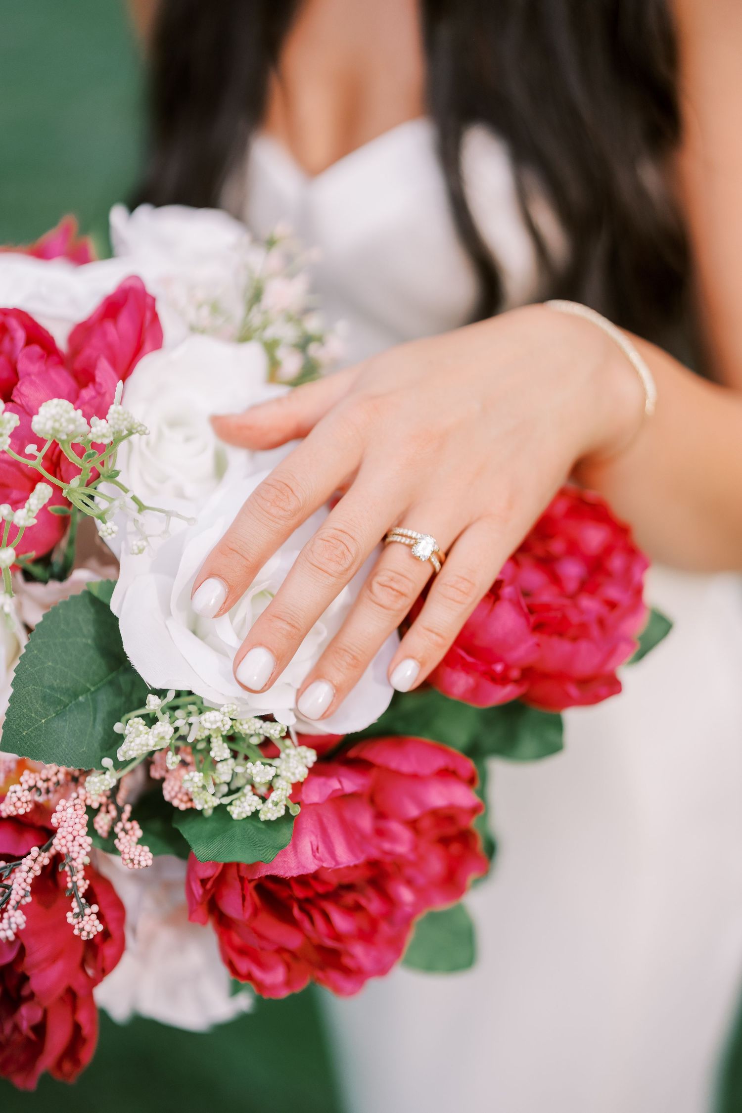 Close-up of bride's hand with wedding ring holding a bouquet of red and white flowers.