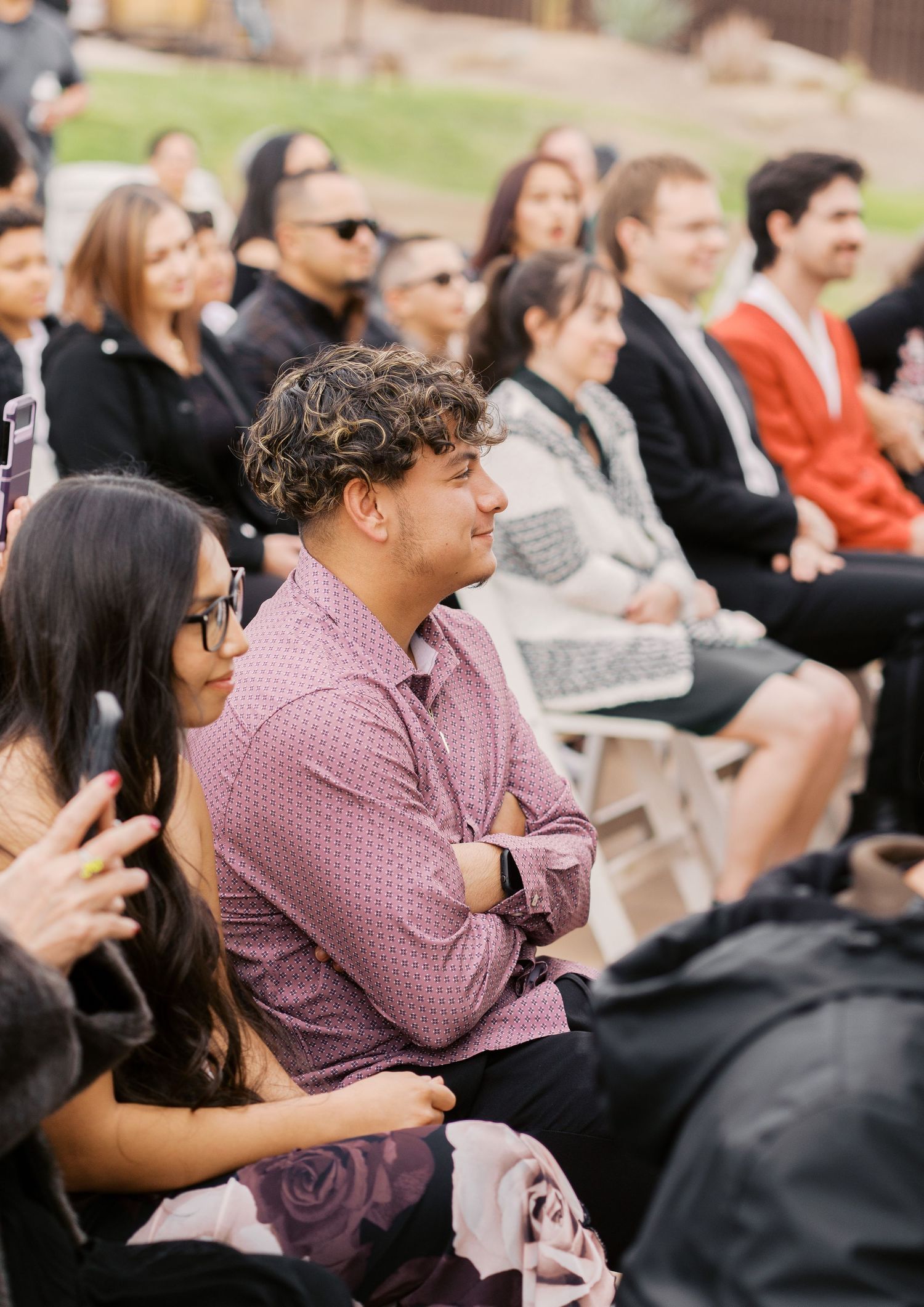A diverse audience sits watching attentively at an outdoor event, with people in casual and business attire in the crowd.