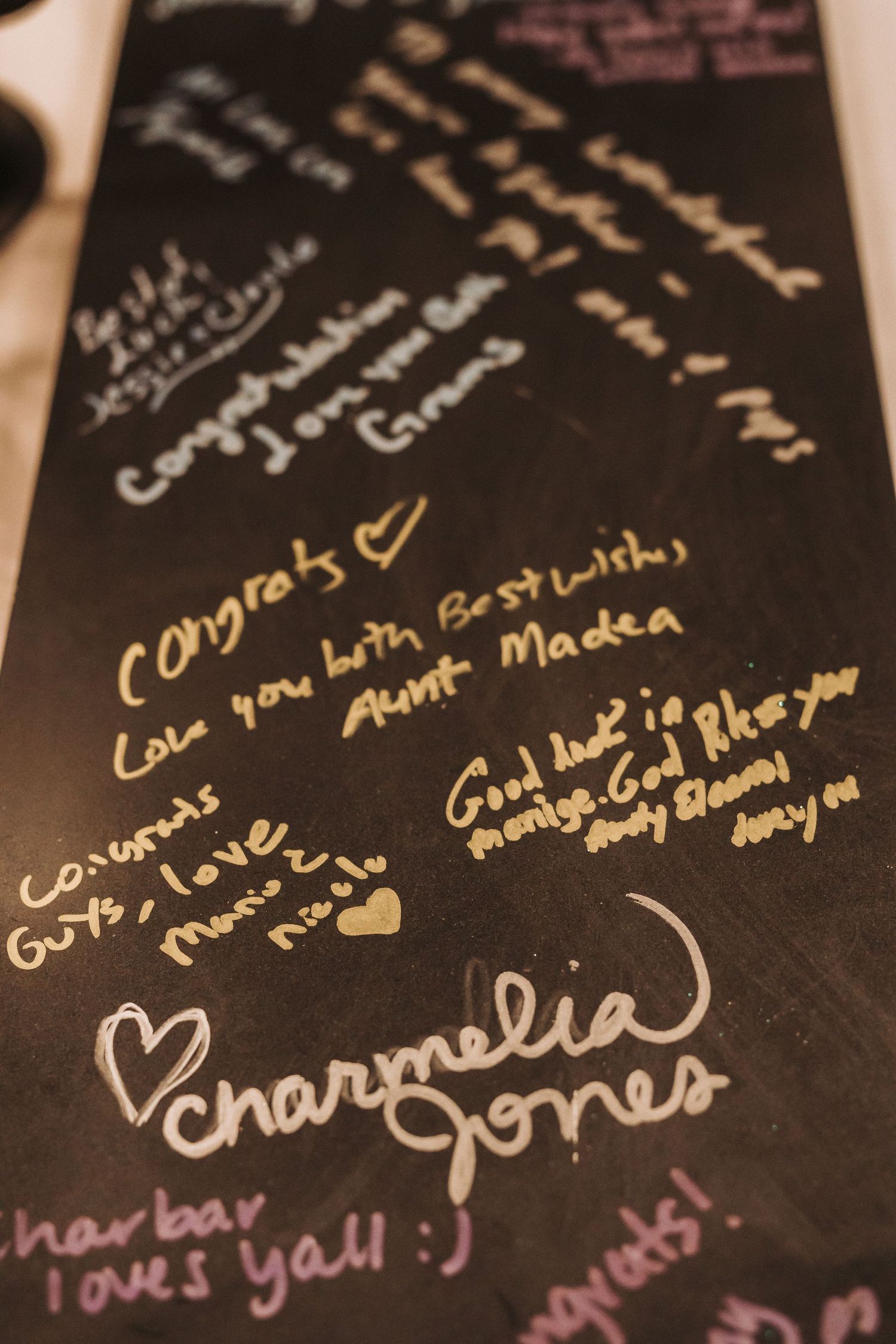 Handwritten messages and signatures in gold and pink ink on a black surface with heart doodles.