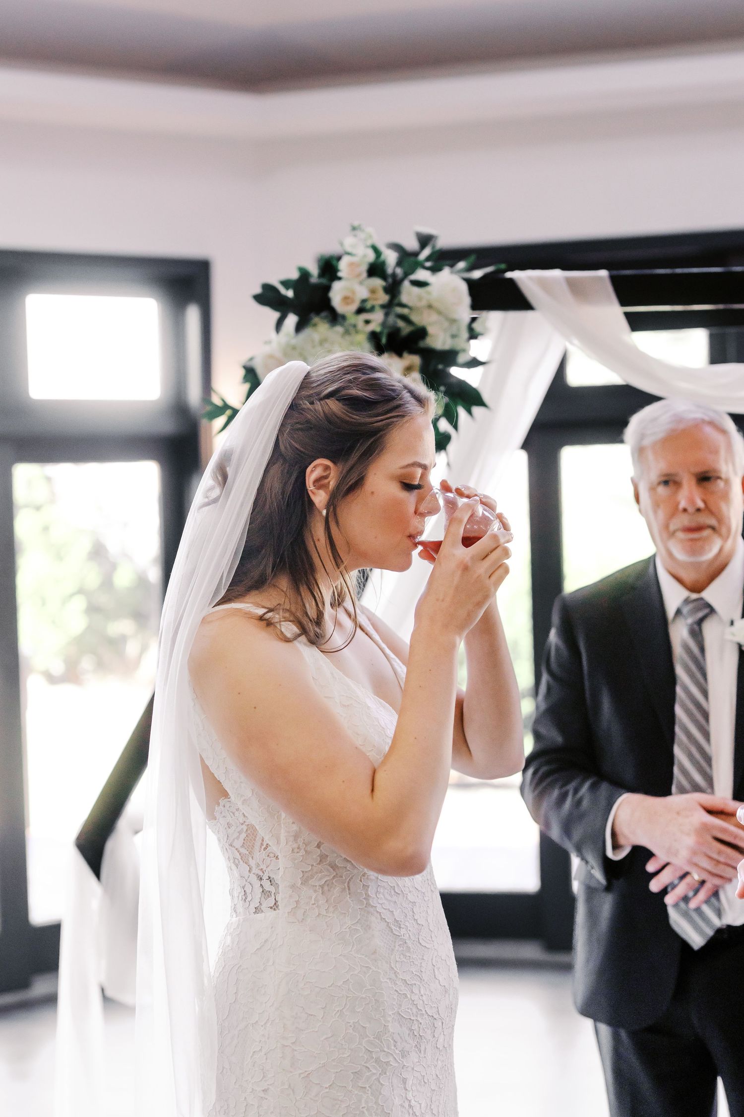 A bride in a lace wedding dress takes a sip of champagne during her wedding ceremony.