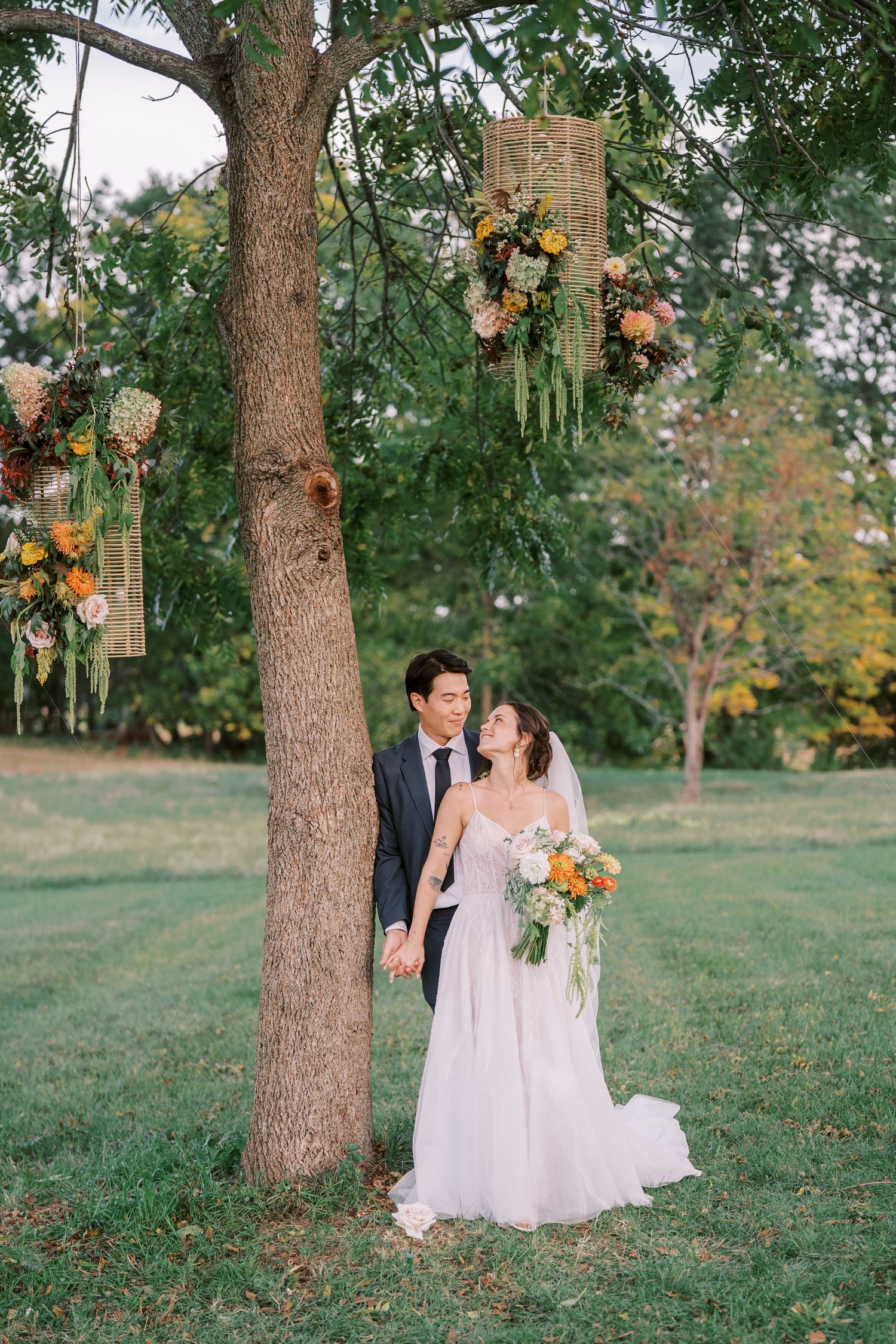 Wedding couple poses under tree decorated with hanging floral arrangements.