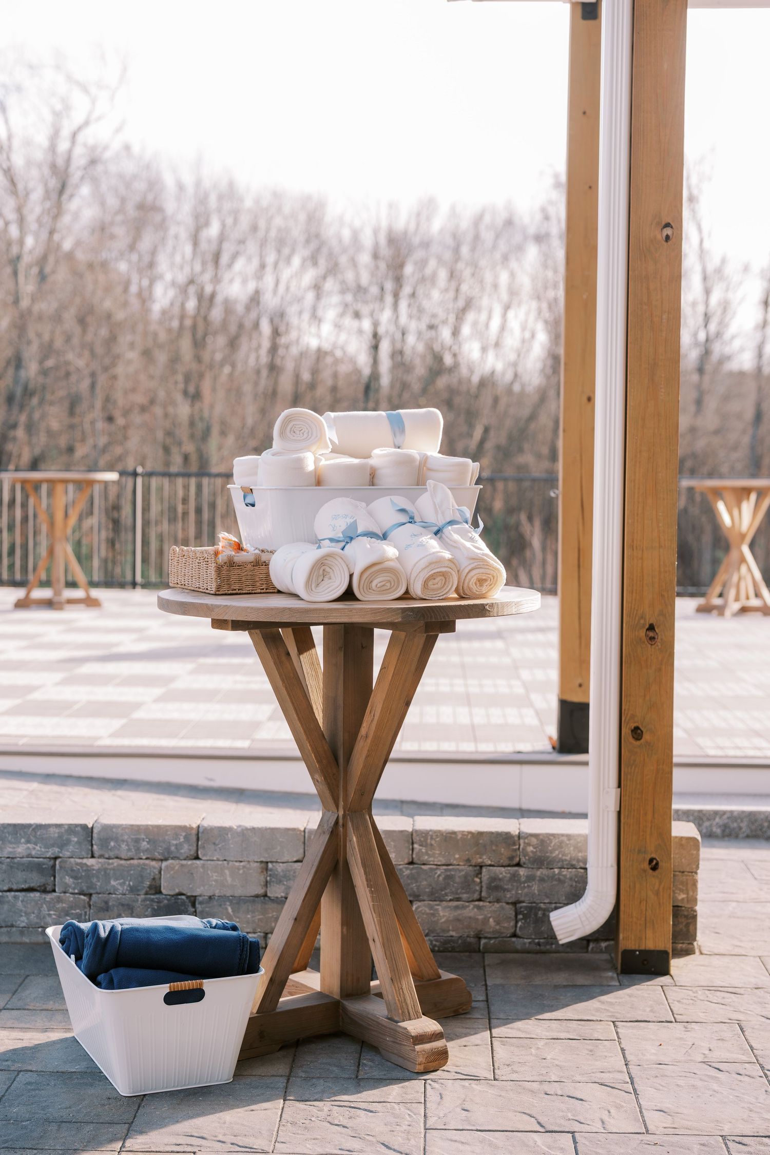 Rustic wooden pedestal tables with white ceramic decor arranged on an outdoor stone patio with snowy landscape views.