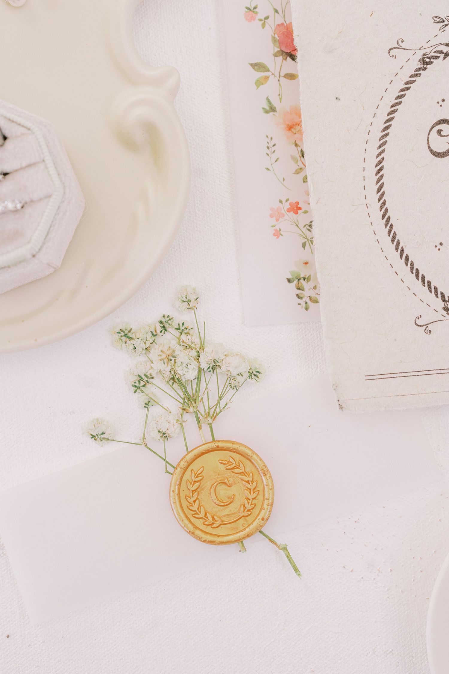 A delicate gold wax seal with small white baby's breath flowers laid on a light textured background.