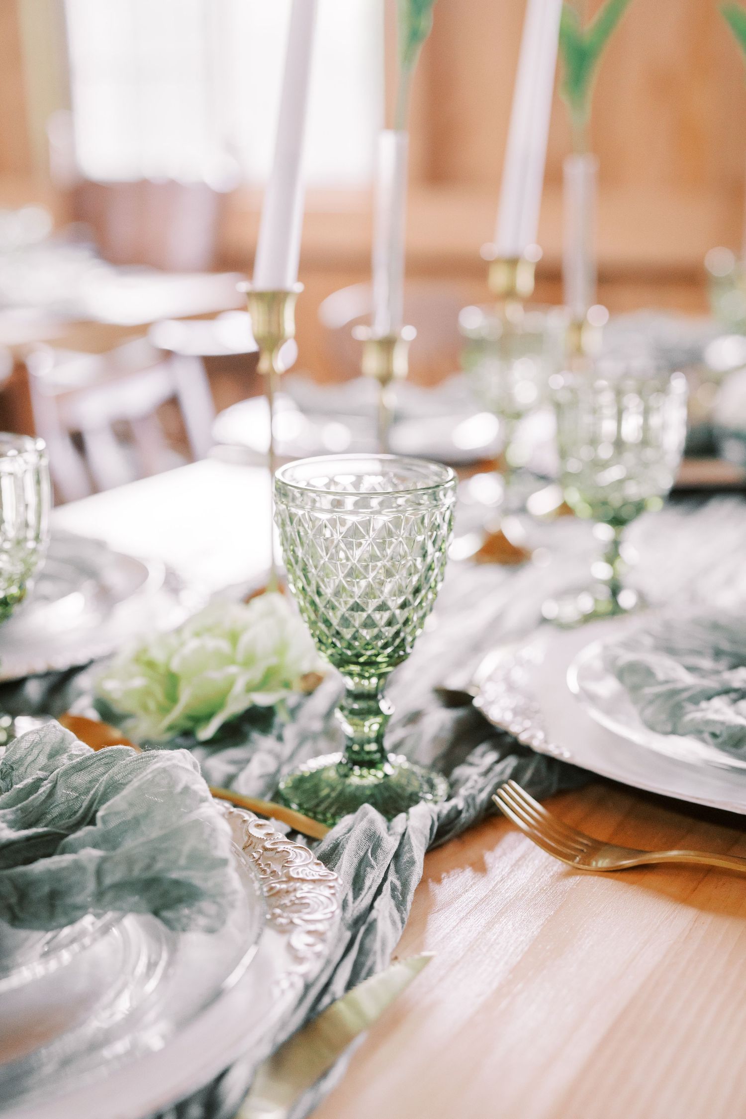 Elegant table setting with vintage green glassware, white plates, and soft sage napkins on a wooden surface.