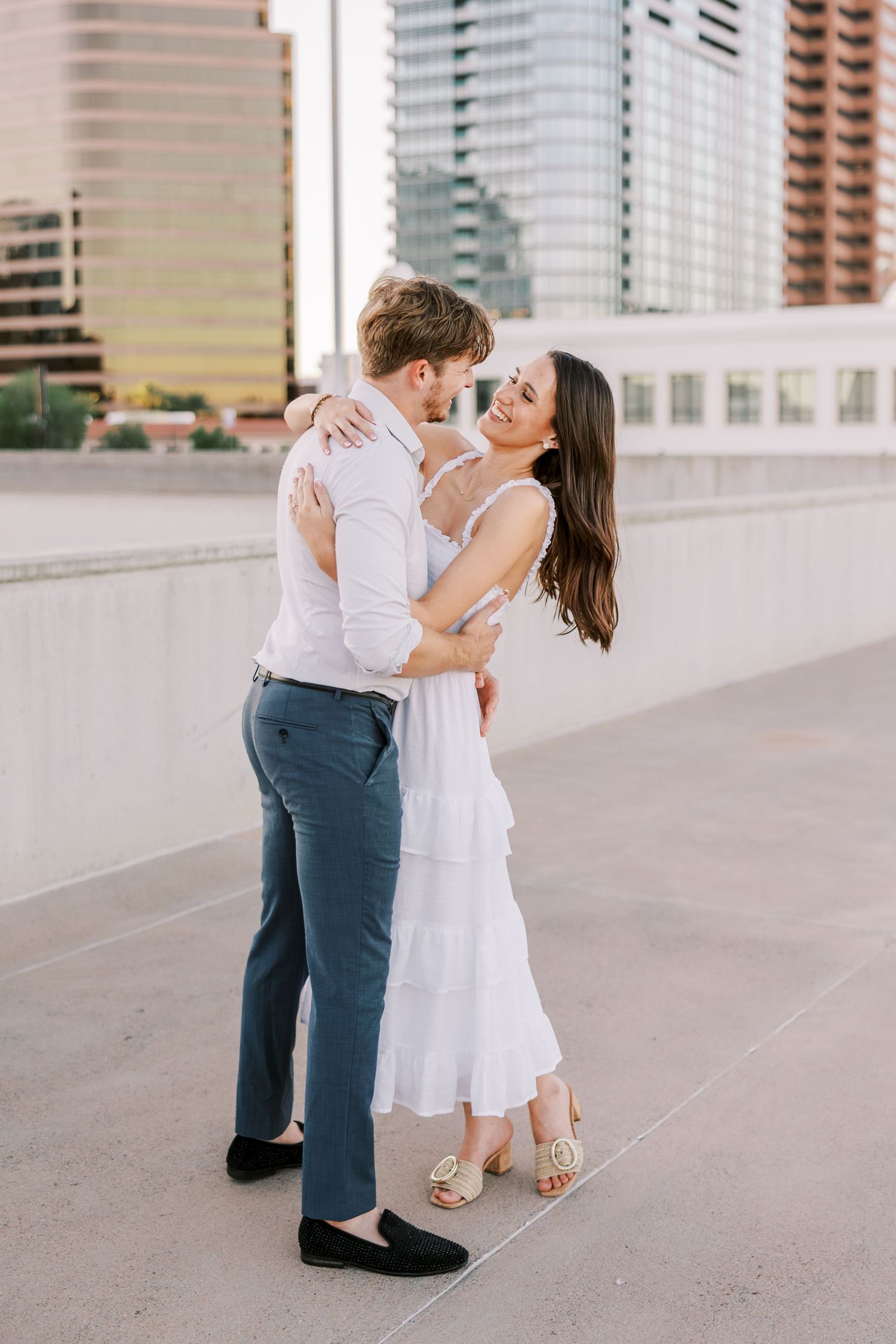 Couple dancing and embracing on urban rooftop with city buildings in background.