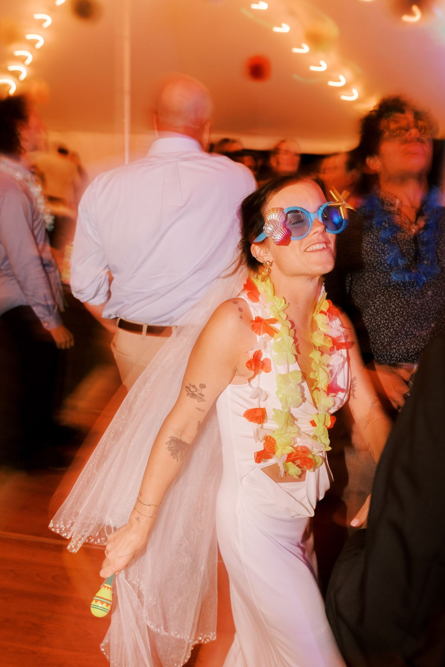 Wedding reception dance floor with motion-blurred dancers in white dresses under warm lighting.