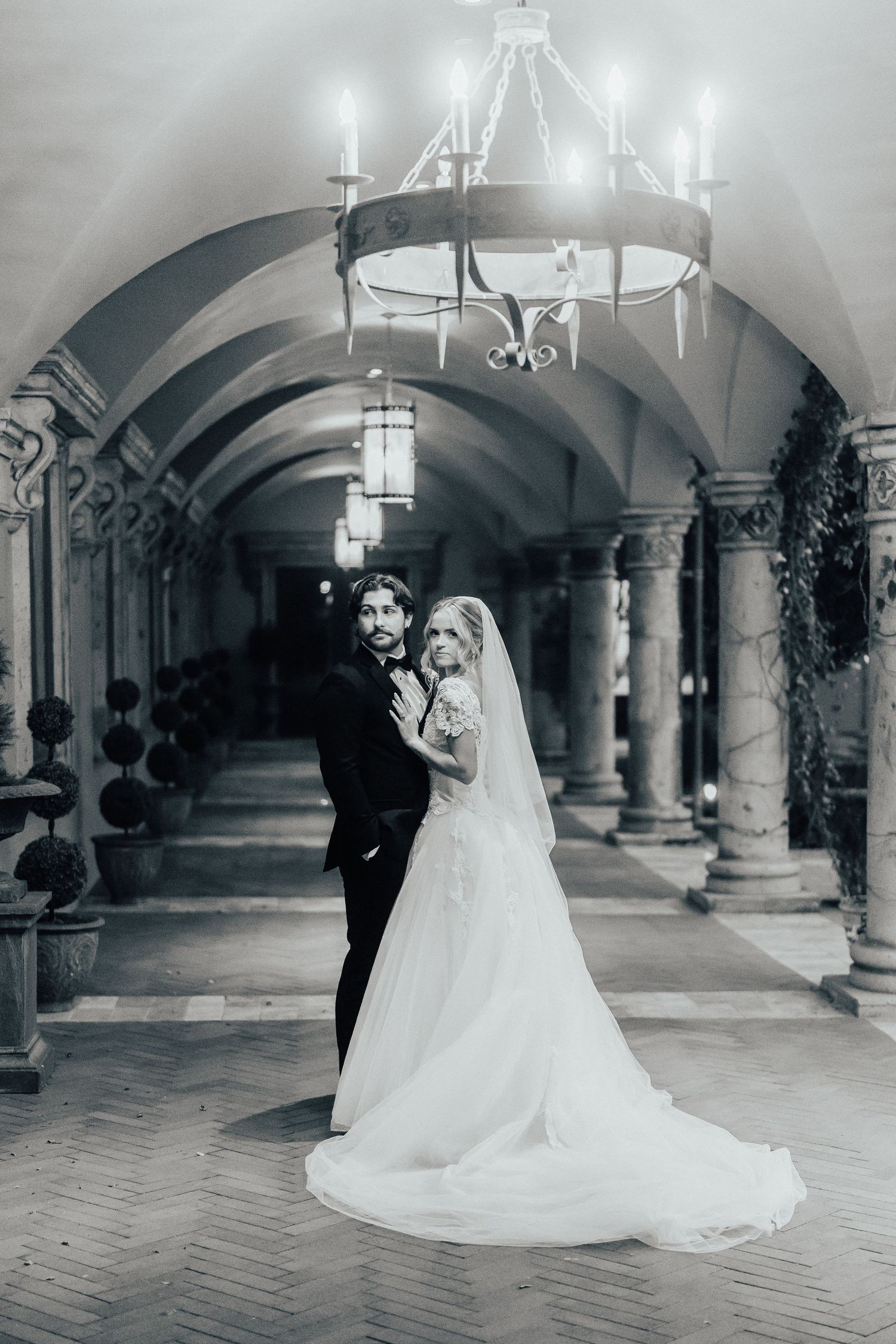 A romantic black and white wedding photo sequence showing a couple in an elegant arched hallway with stone columns.