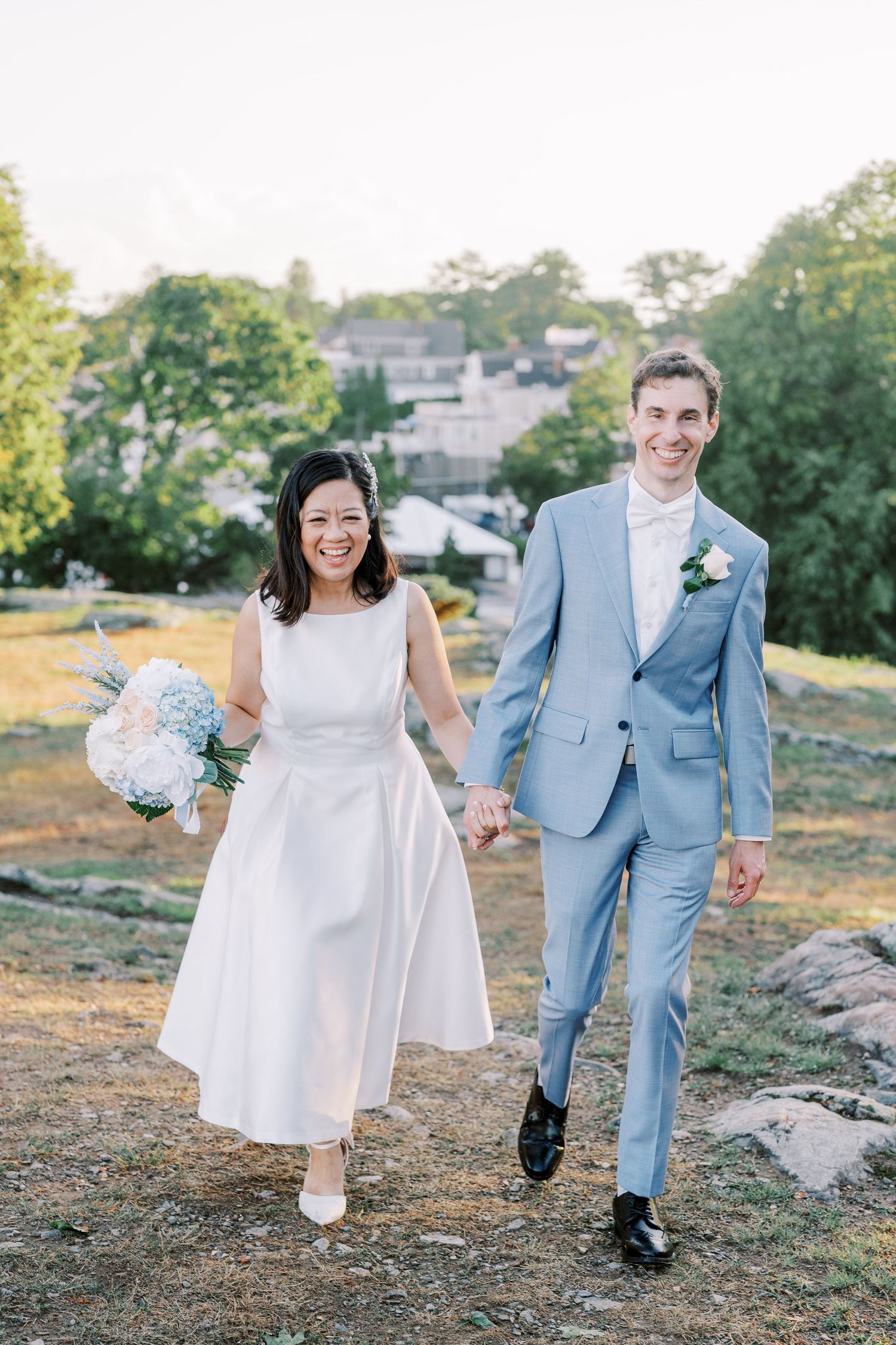 Wedding couple walking and laughing together on rocky terrain during golden hour.