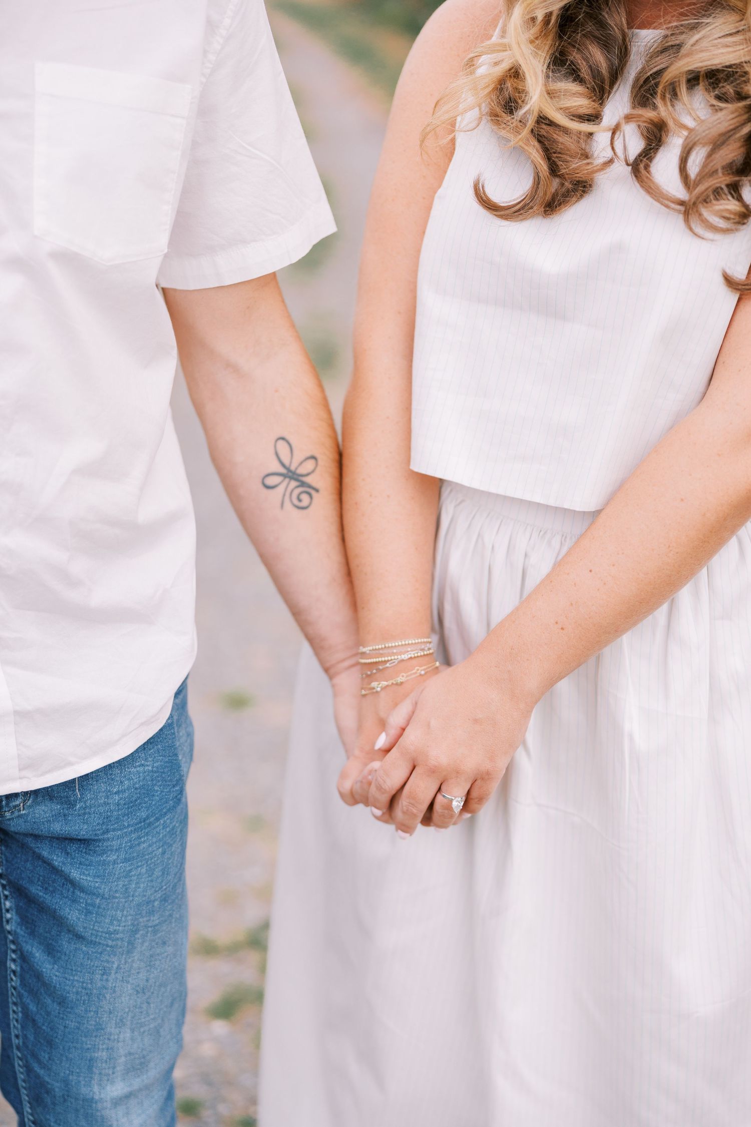A couple in white outfits holding hands intimately in an outdoor setting.