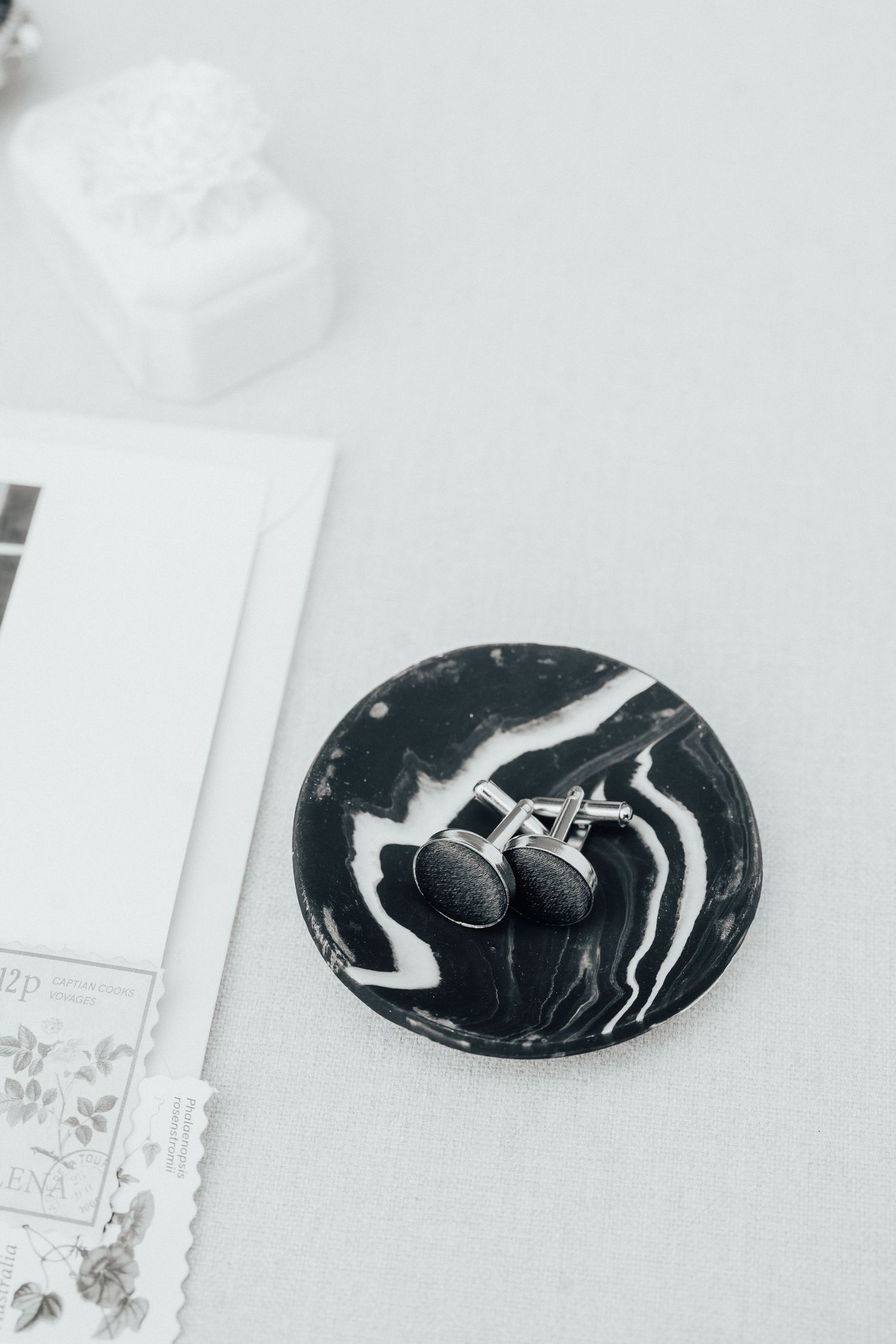 Black and white marbled plate holding elegant earrings beside stationery and a white box.