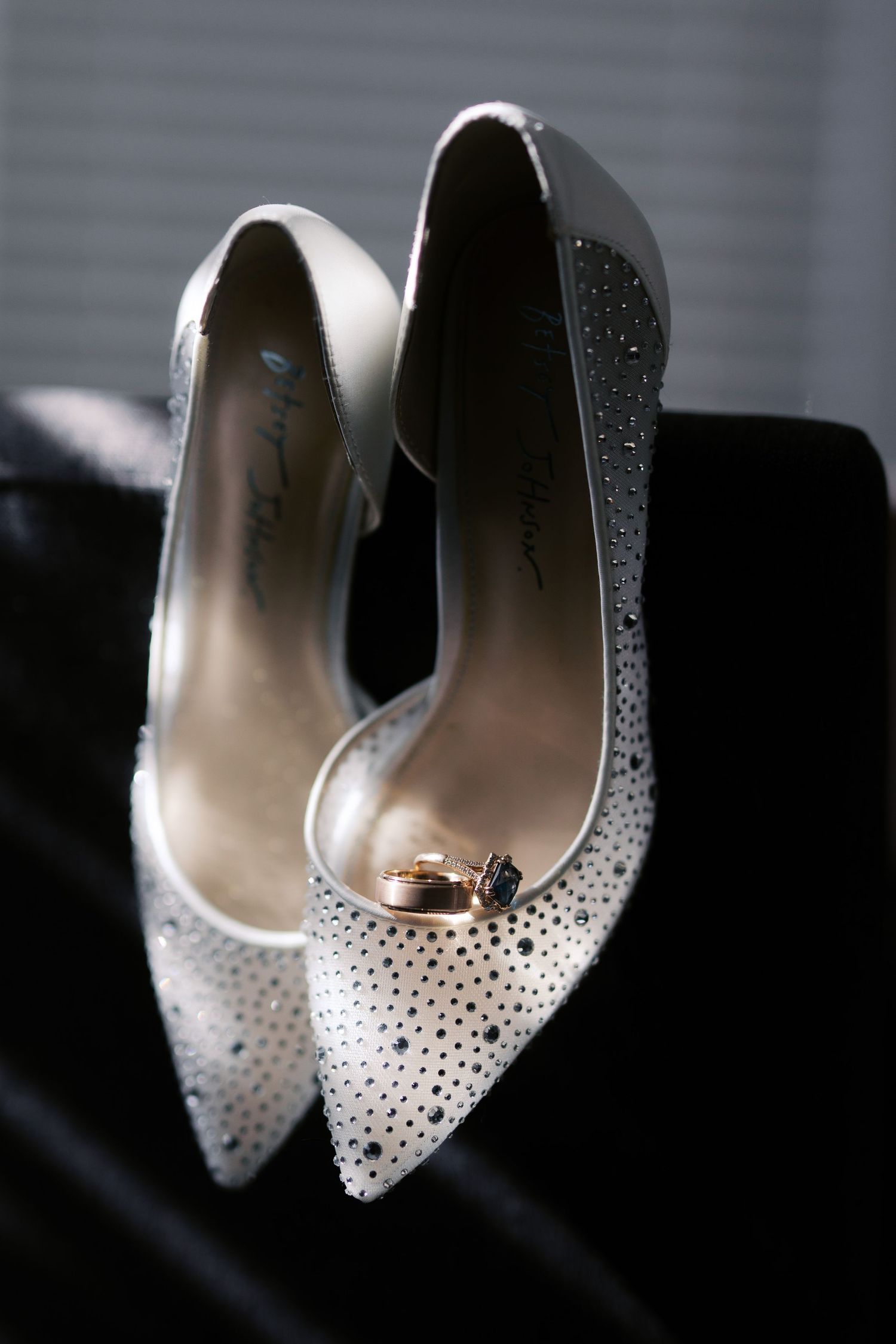 Elegant white bridal shoes with sparkling crystal embellishments displayed against a dark background.
