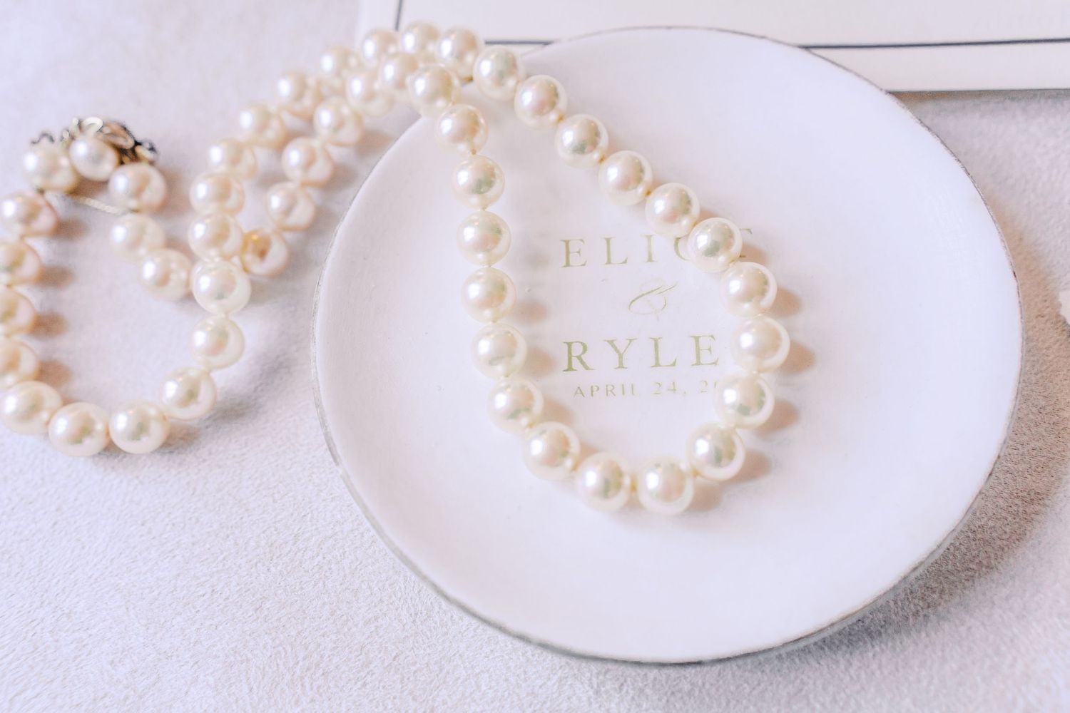 Pearl necklaces arranged in circular patterns on white ceramic plates with elegant lettering.