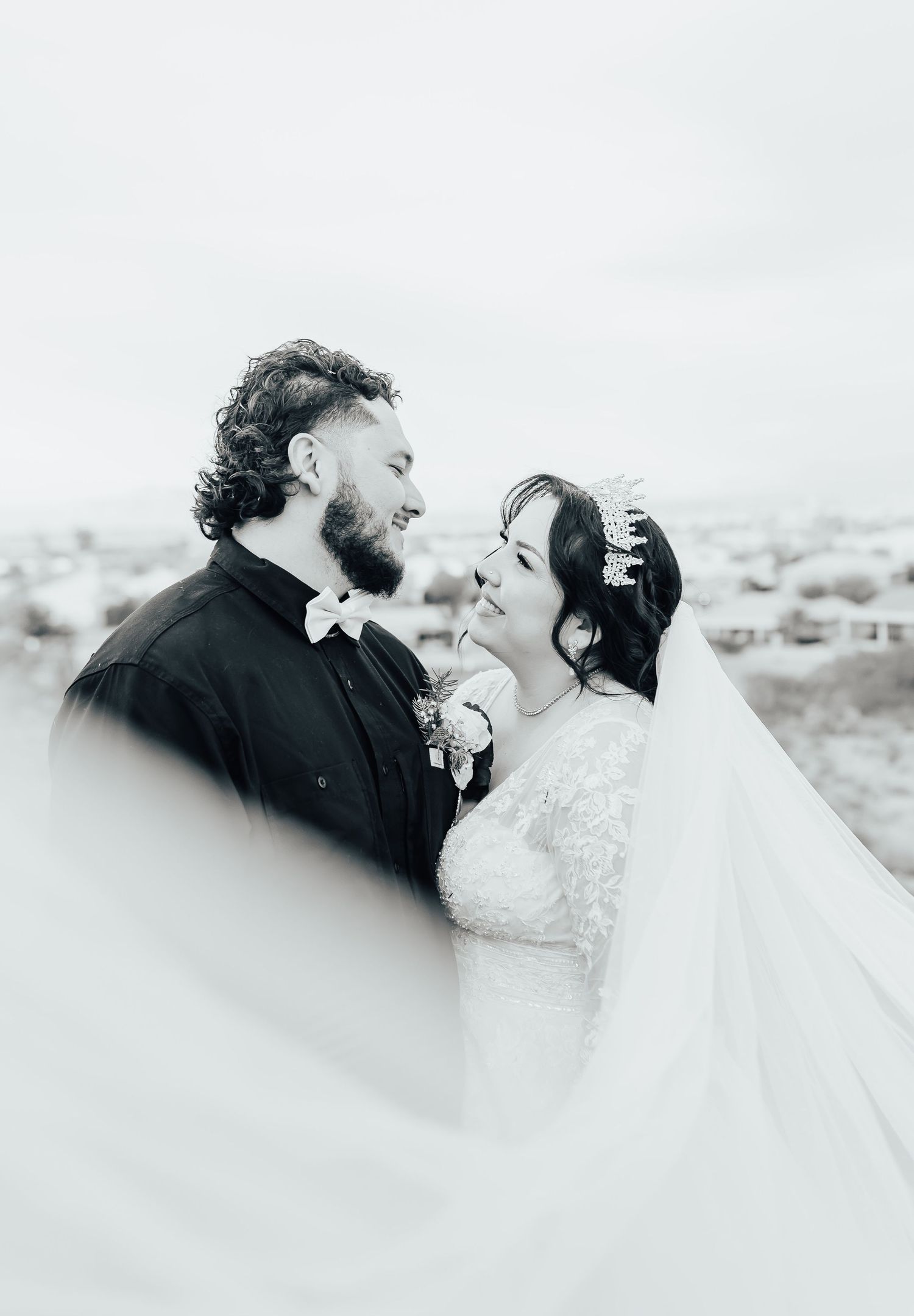 Black and white wedding portrait of a bride and groom sharing an intimate moment outdoors with a flowing veil.