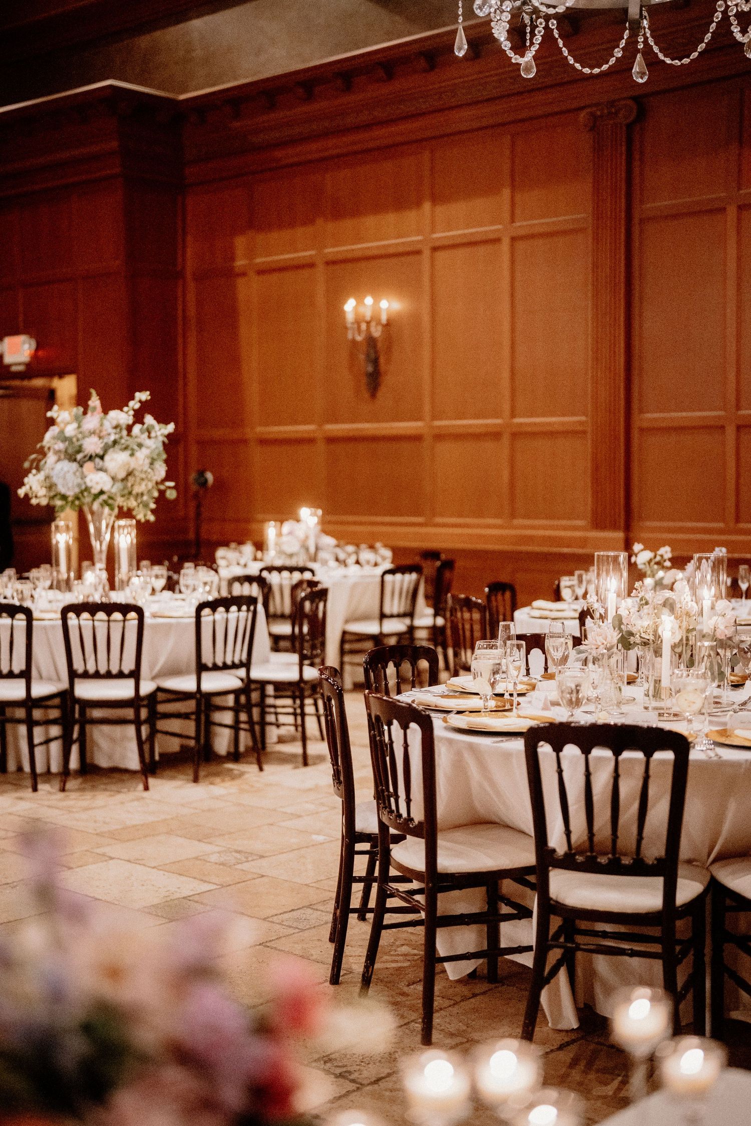 Elegant wedding reception venue with dark wooden chairs and white tablecloths illuminated by romantic candlelight.