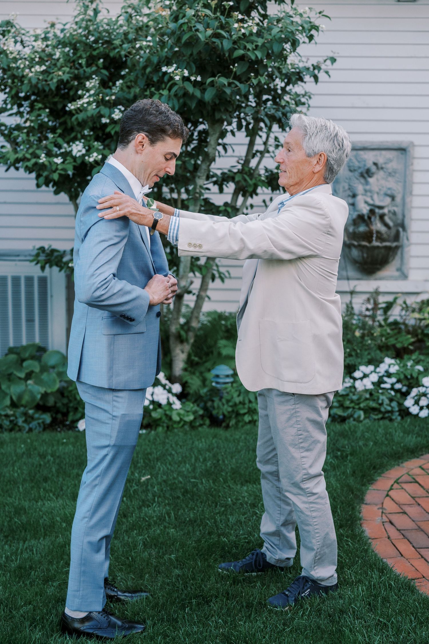Two men in suits sharing a heartwarming moment in a garden setting.