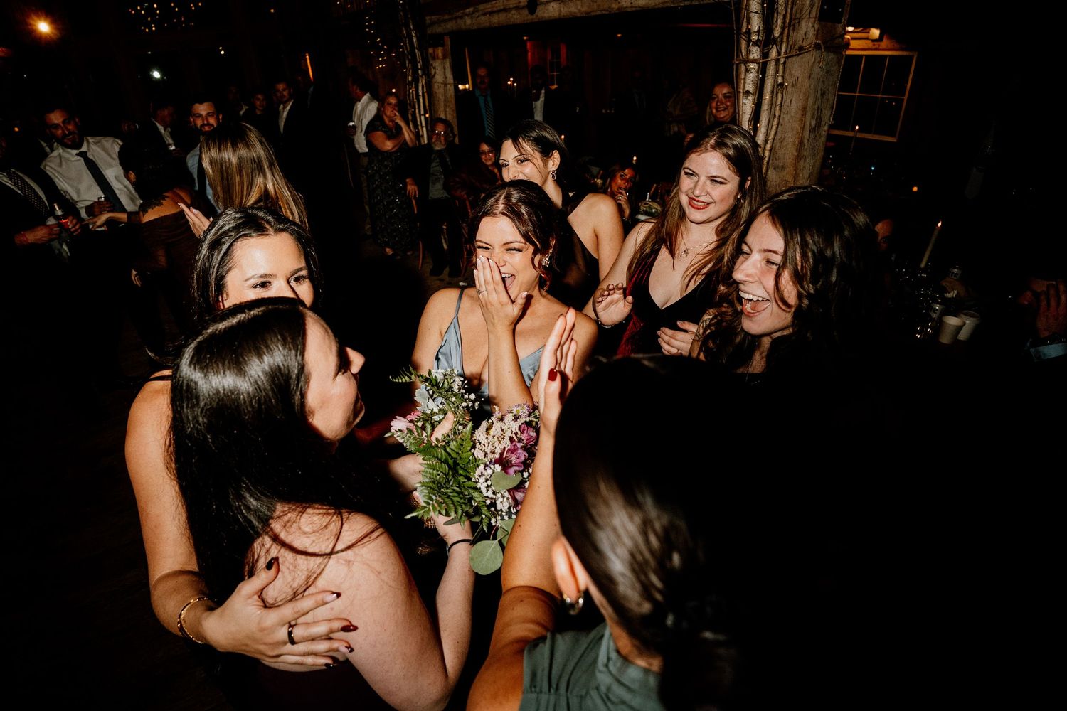 A group of friends laughing and dancing together at a dimly lit nighttime celebration.