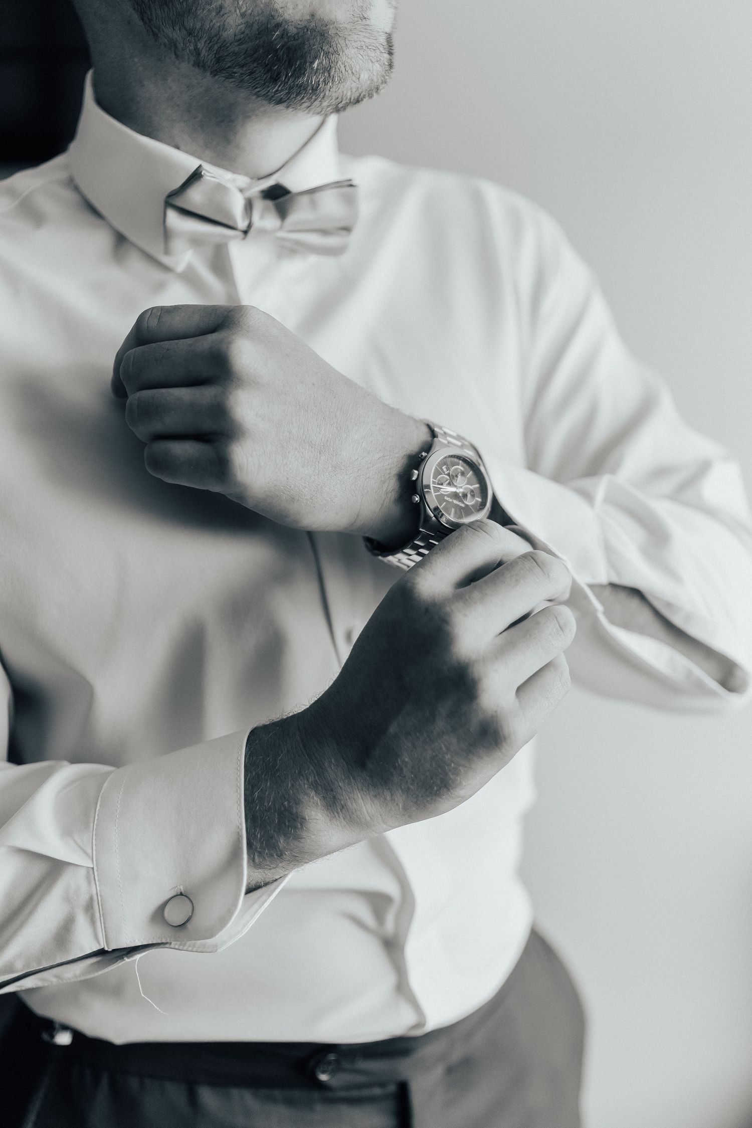 Close-up black and white images of someone adjusting a white dress shirt cuff and watch in multiple poses.