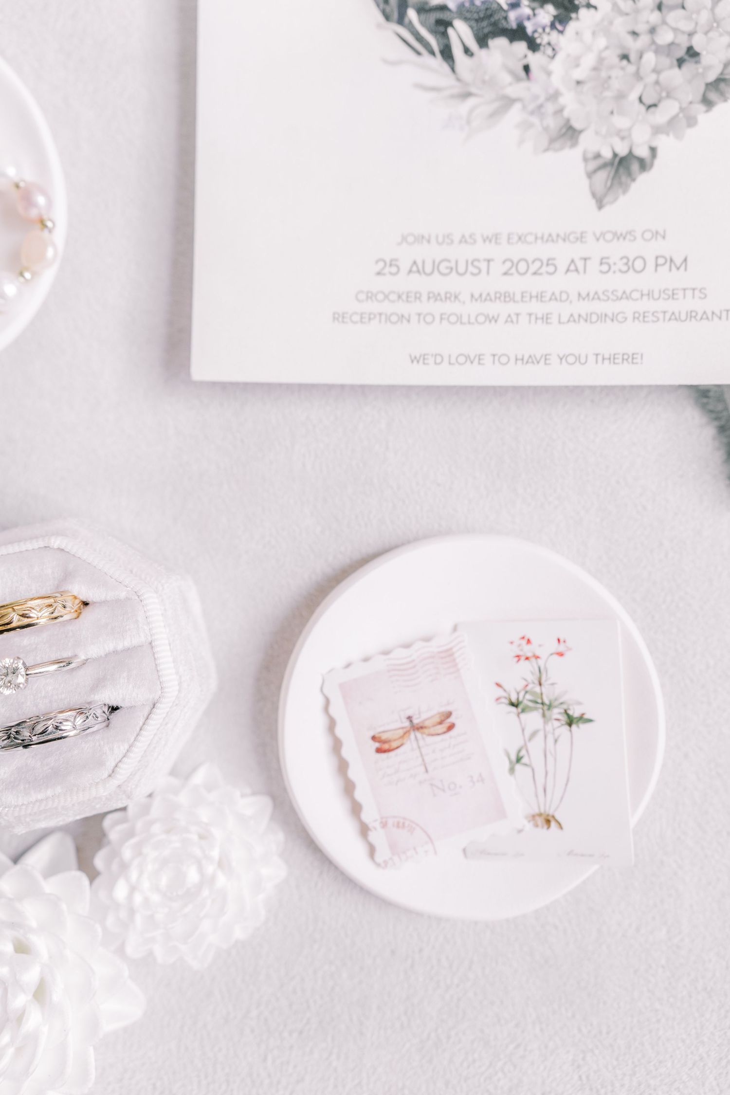 Wedding invitation and delicate floral artwork displayed on white ceramic plates.