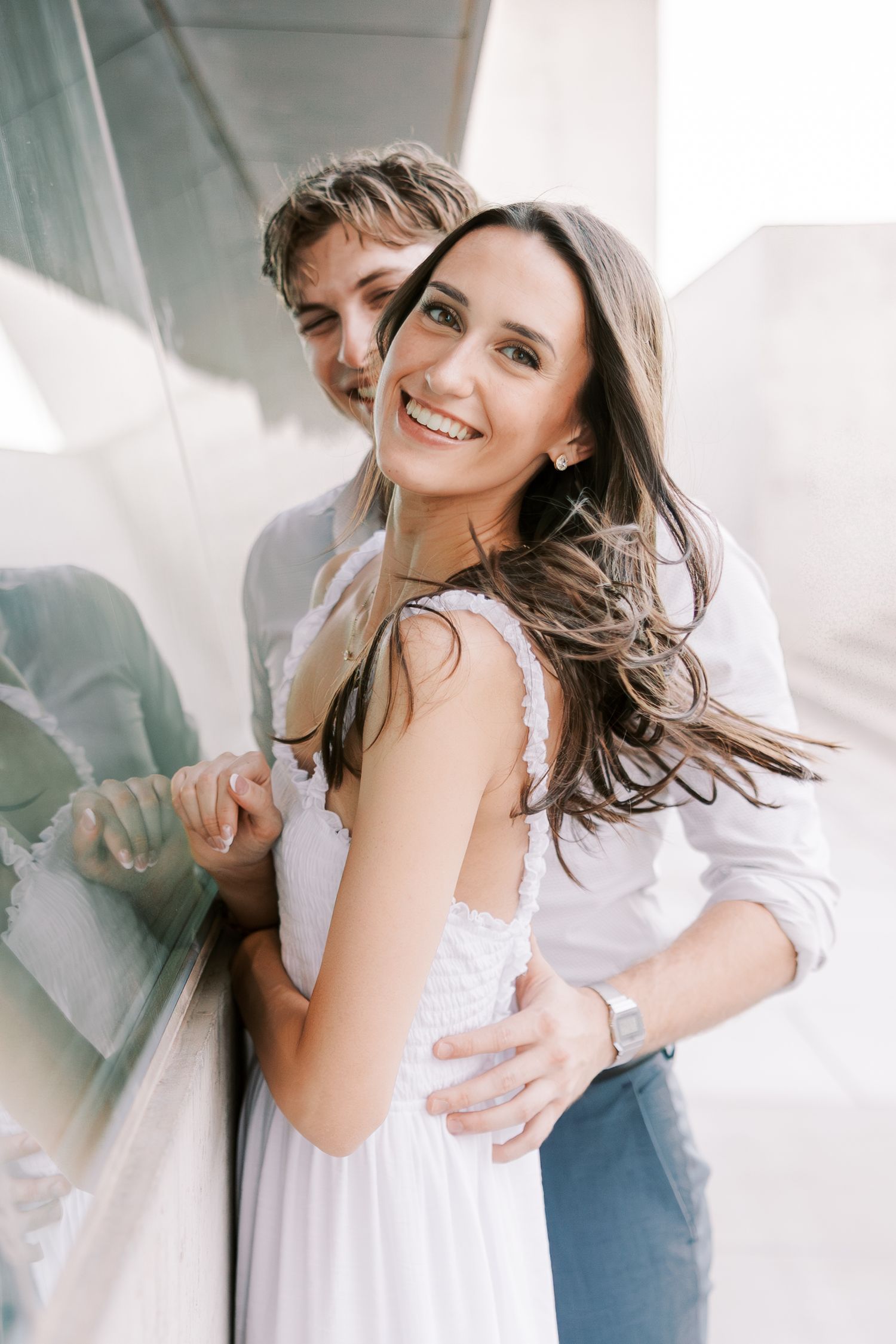 Couple sharing intimate moments in white outfits against bright architectural backdrop.