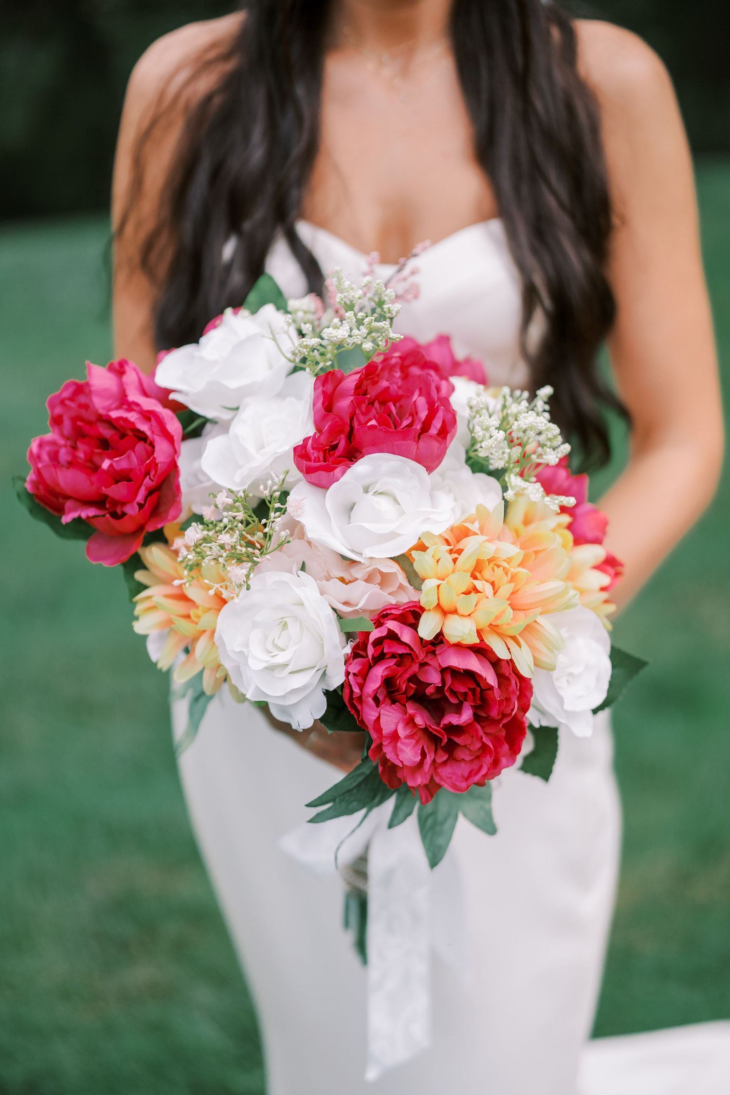 A stunning bridal bouquet featuring pink peonies, white roses, and peach dahlias held against a white wedding dress.