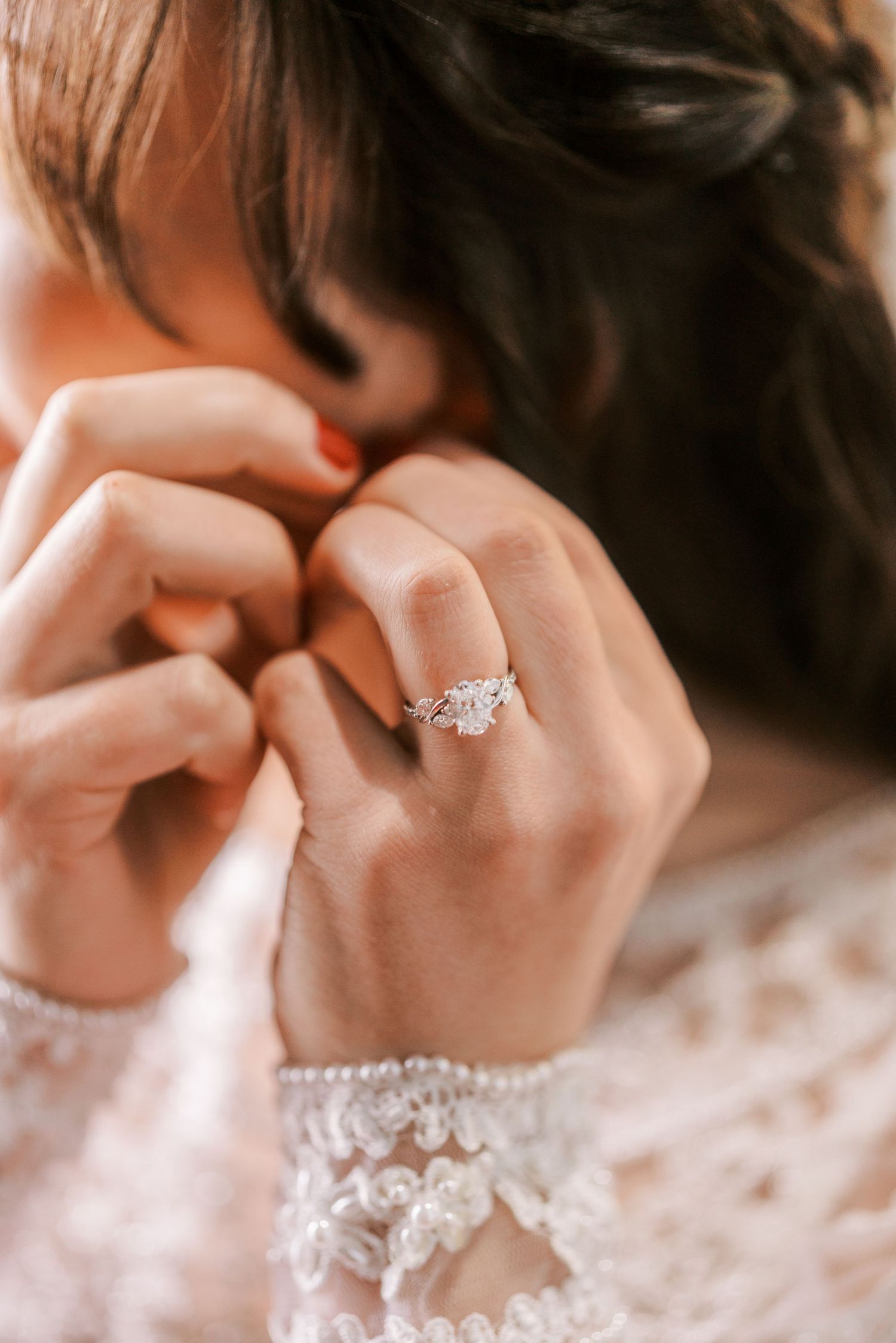 Close-up shot of hands wearing delicate white lace while displaying an elegant diamond engagement ring.