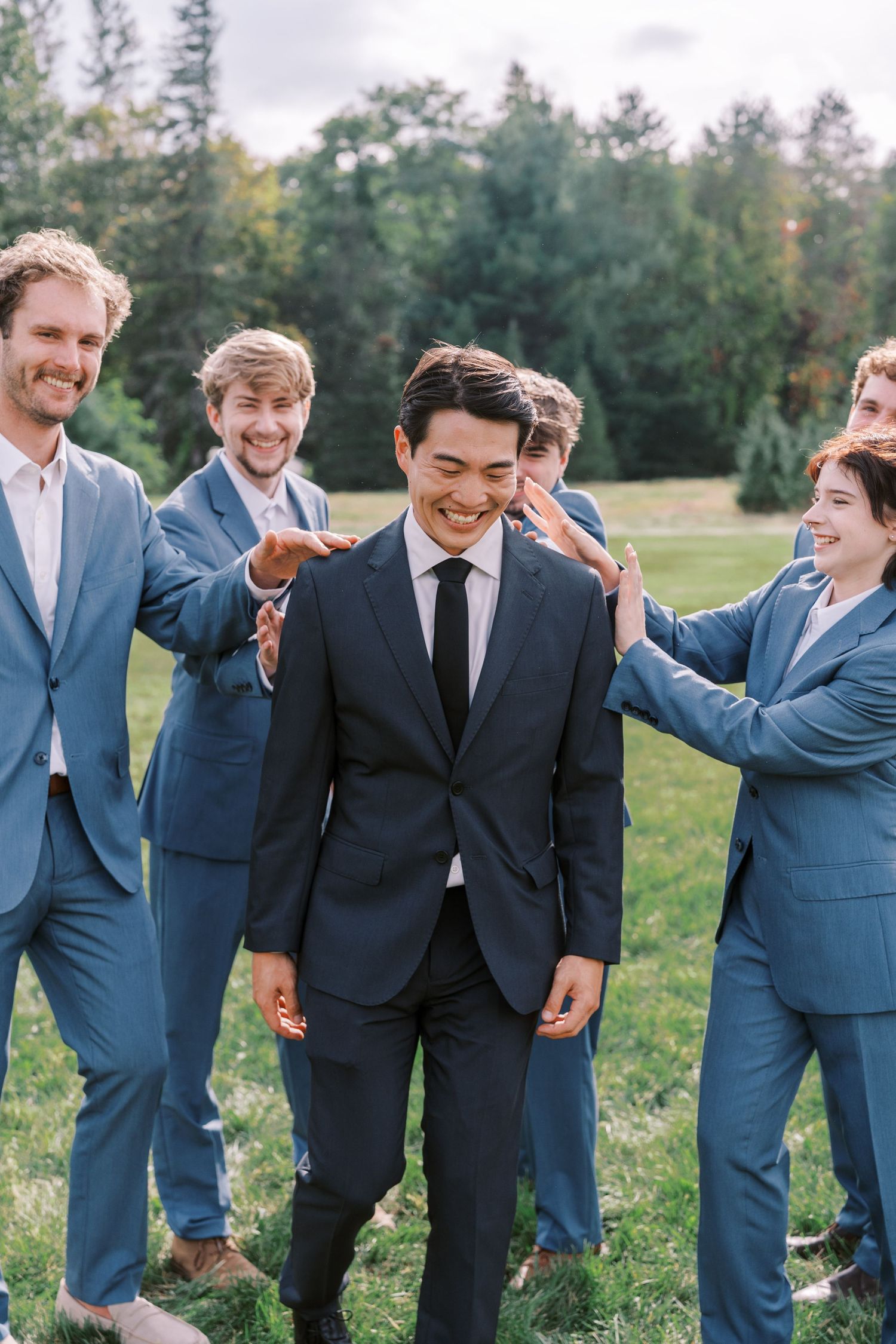 Groomsmen in blue suits share a joyful moment during outdoor wedding photos.
