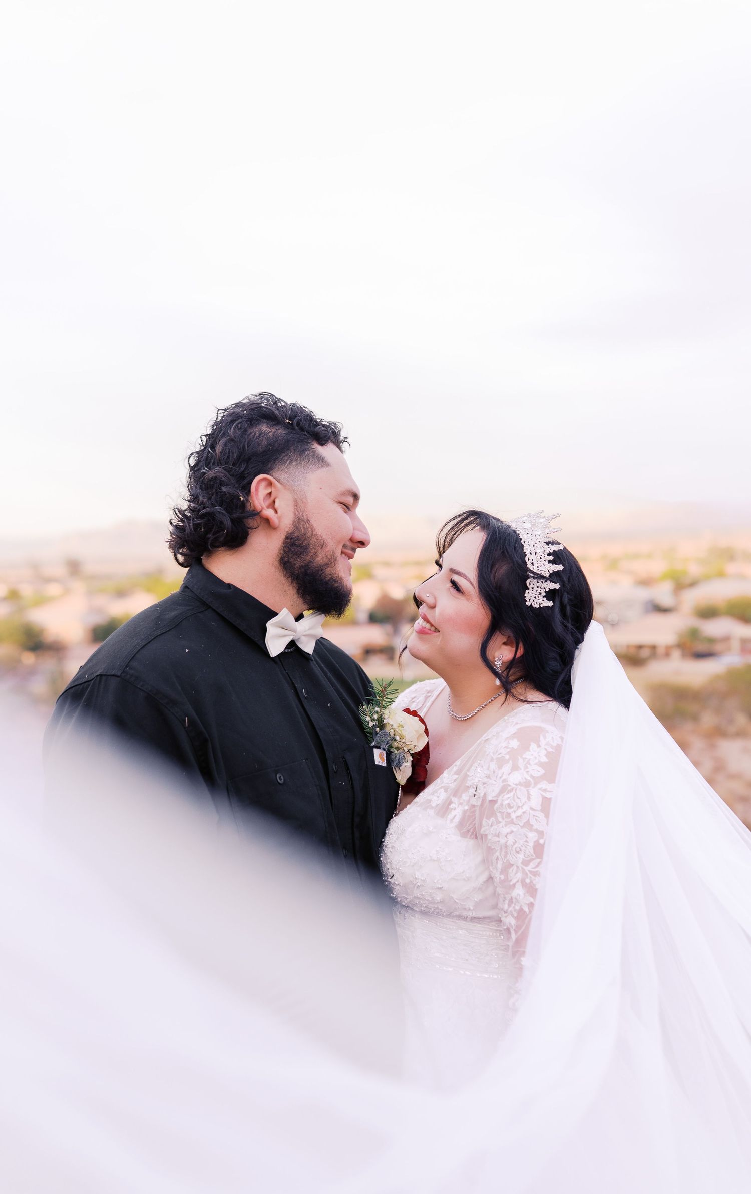 A couple shares a romantic moment in formal wedding attire against a desert landscape background.