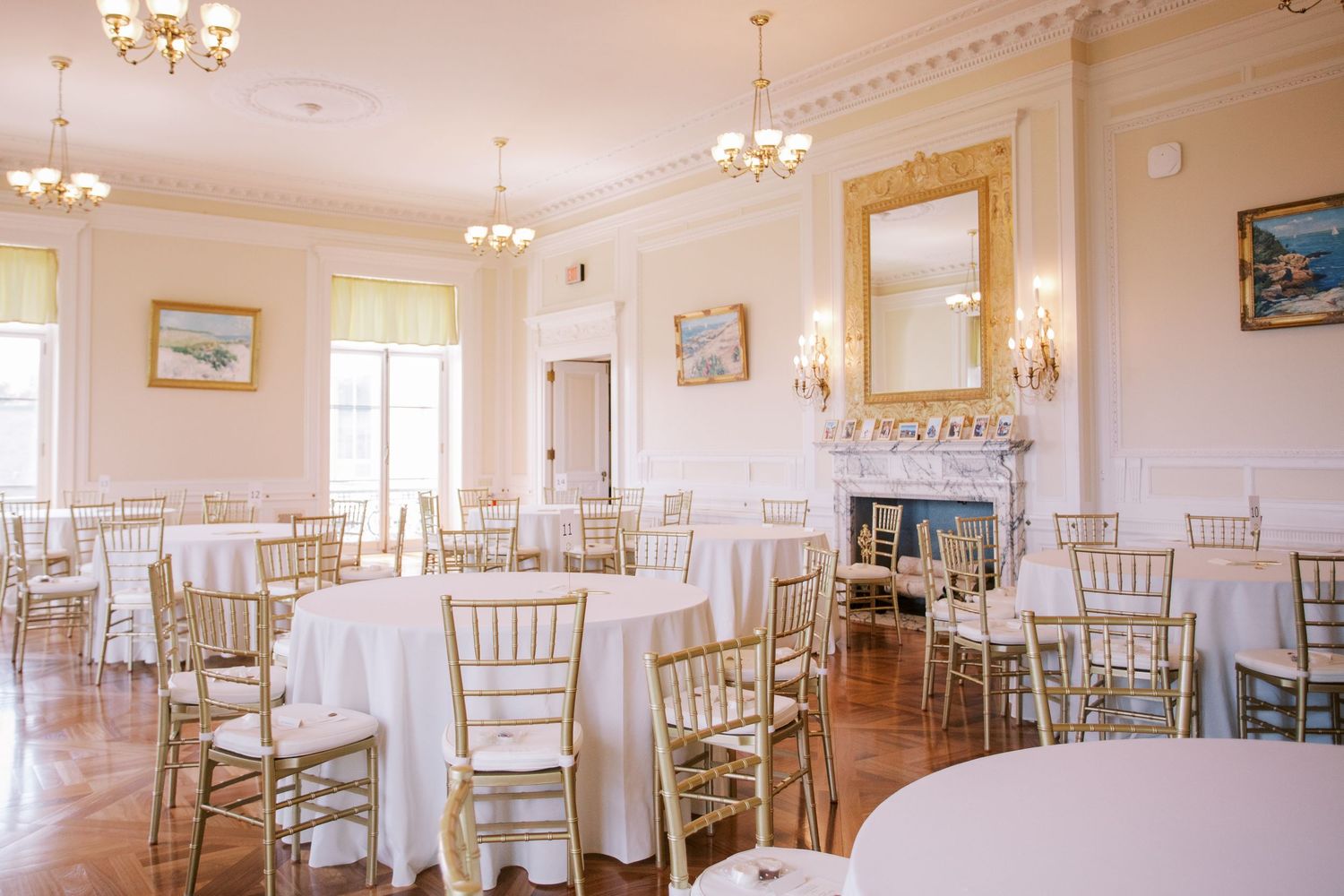 Elegant reception hall with crystal chandeliers and white chiavari chairs arranged for a wedding celebration.