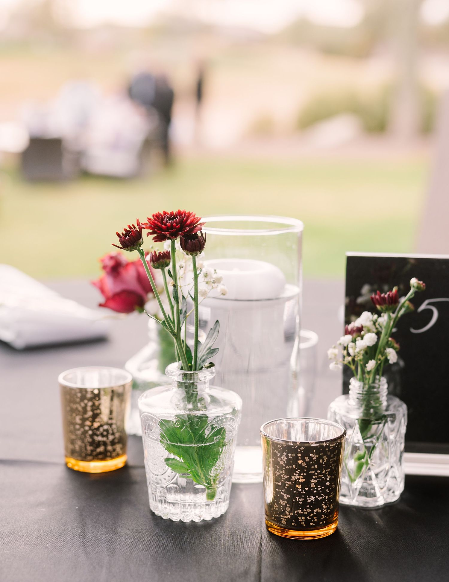 Elegant table setting with red carnations in crystal vases and gold-trimmed votives on a dark surface with table number.