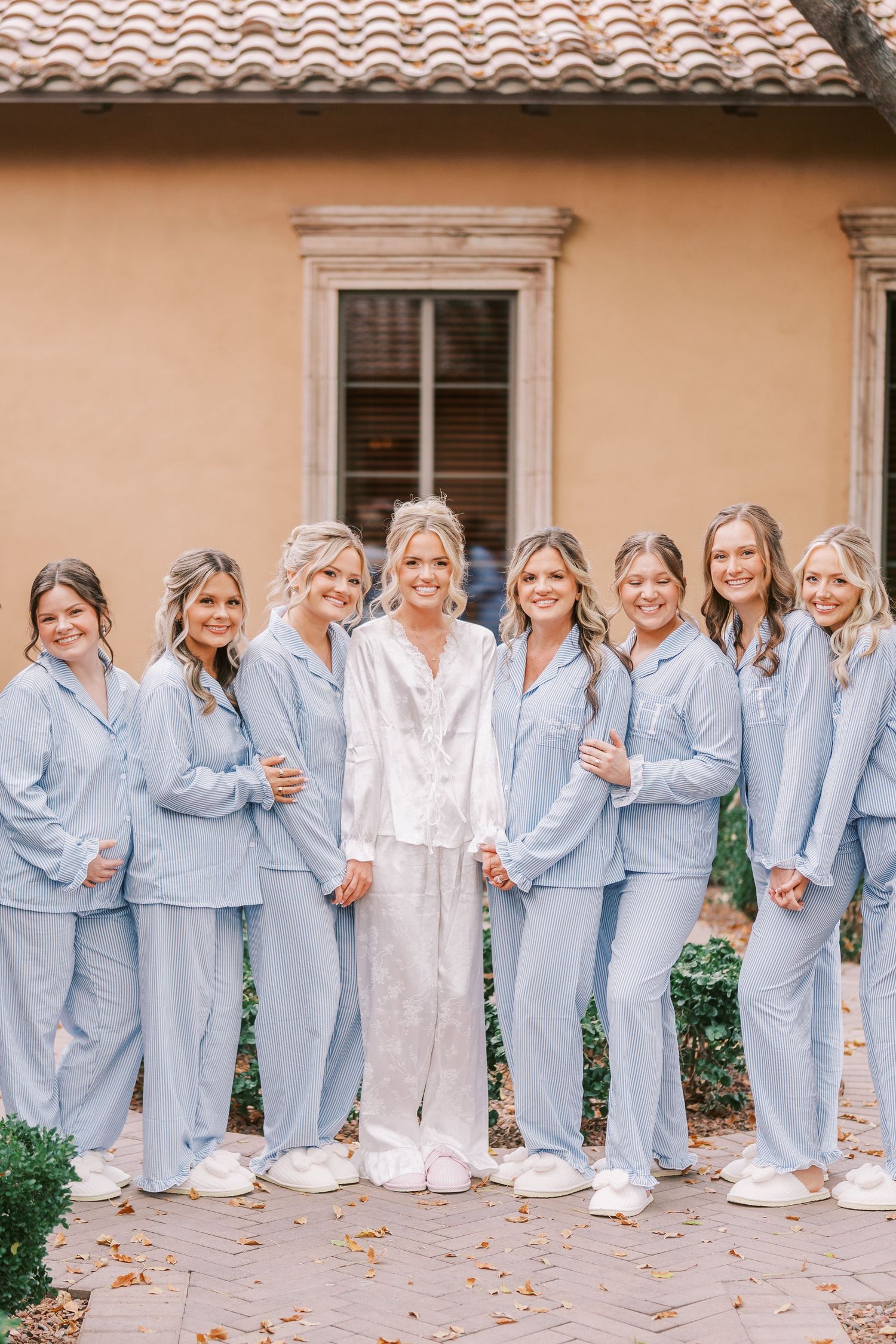 Bridesmaids wearing matching blue pajamas pose together with bride in white robe during wedding morning preparations.