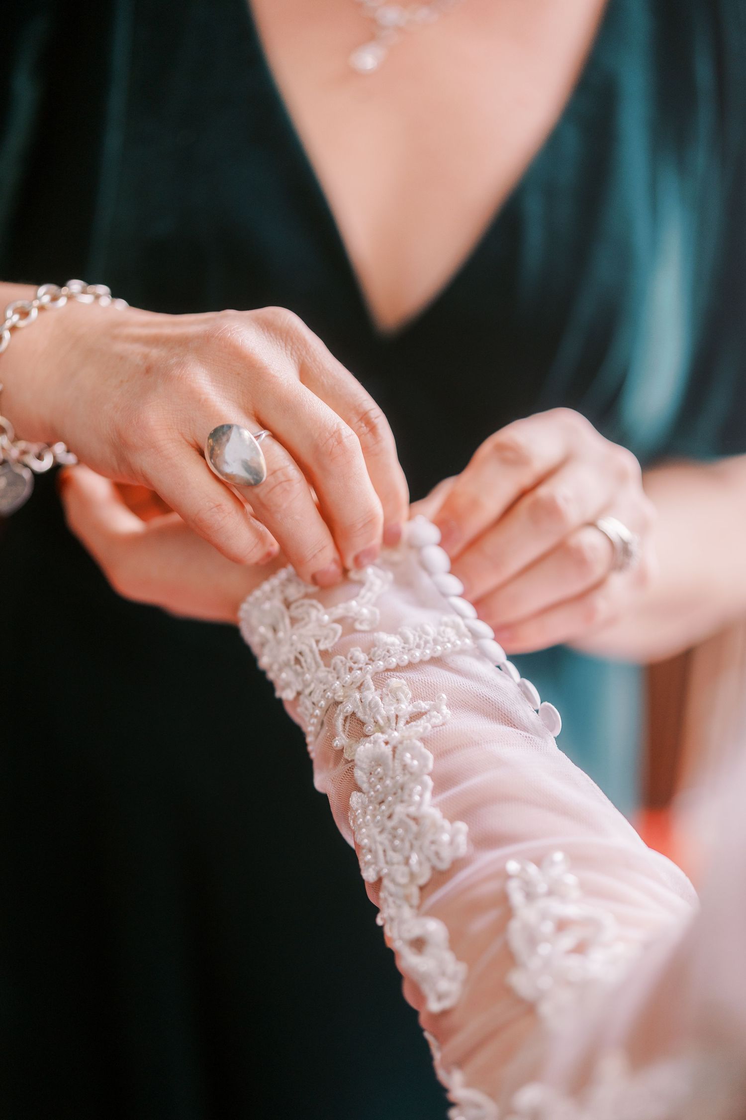 Close-up of hands fastening delicate lace details on white wedding attire.