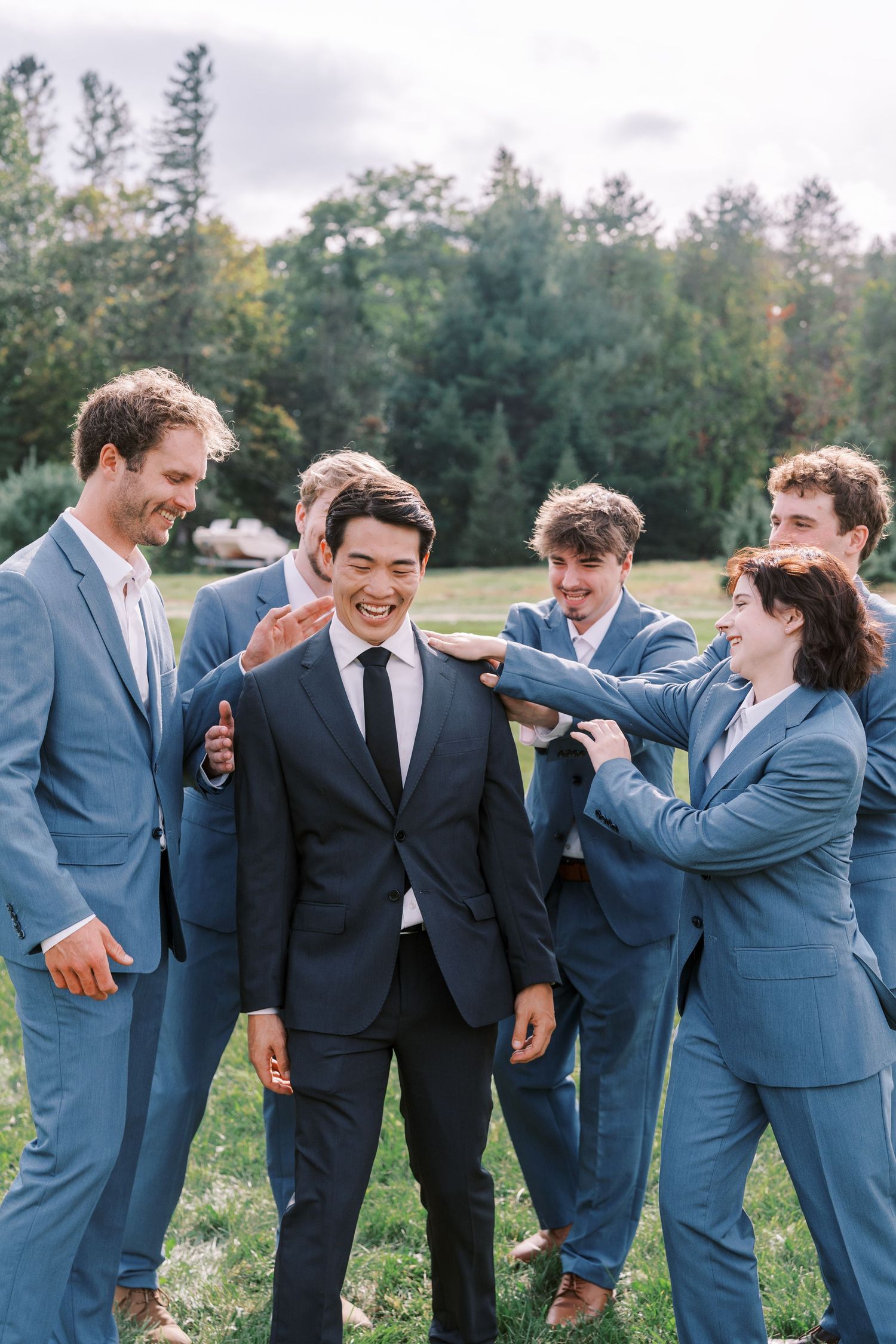 Wedding party in blue suits share candid laughing moments during outdoor photo session.