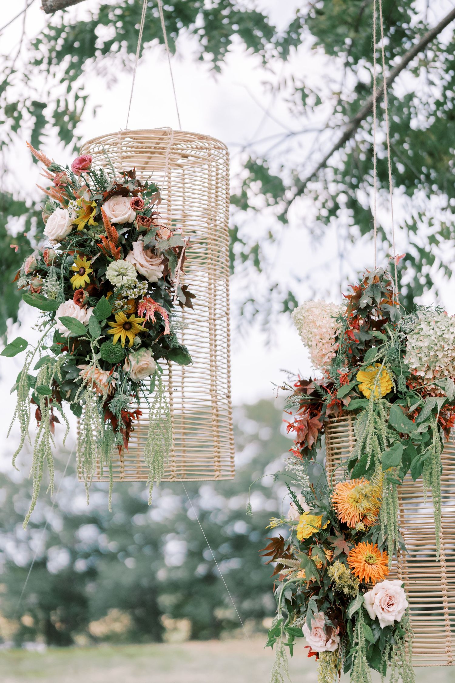 Hanging wicker lanterns decorated with lush floral arrangements featuring orange, pink and green blooms outdoors.