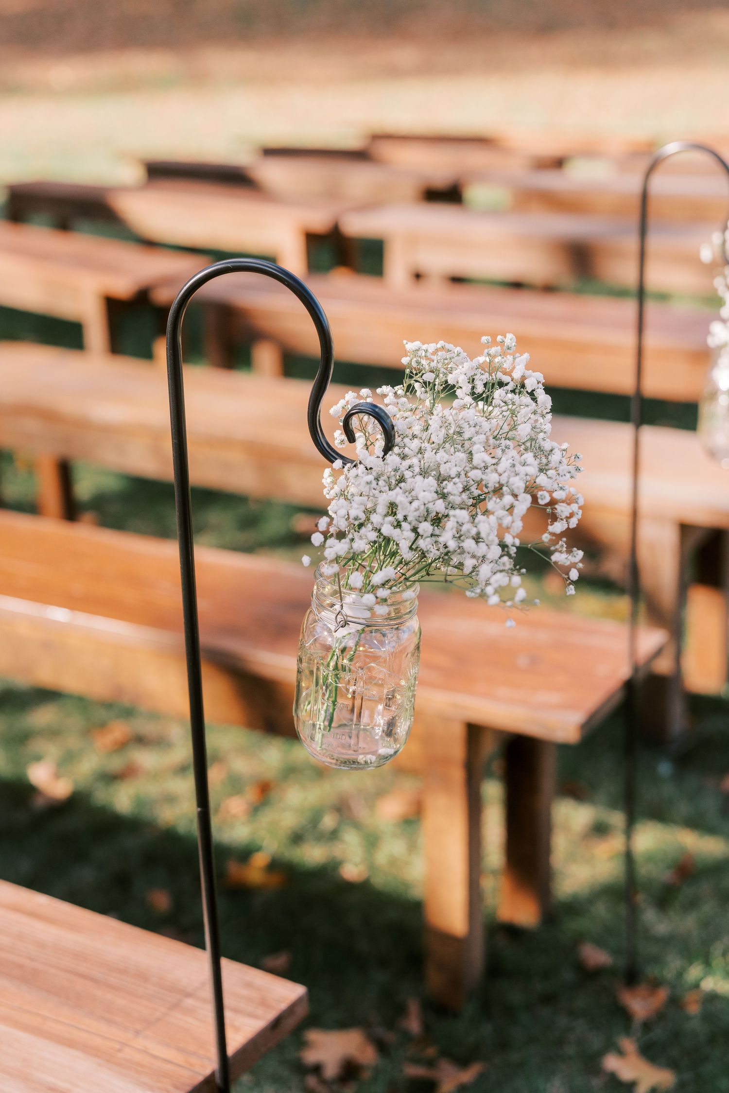 Rustic wooden benches with mason jars filled with baby's breath flowers line an outdoor wedding ceremony aisle.