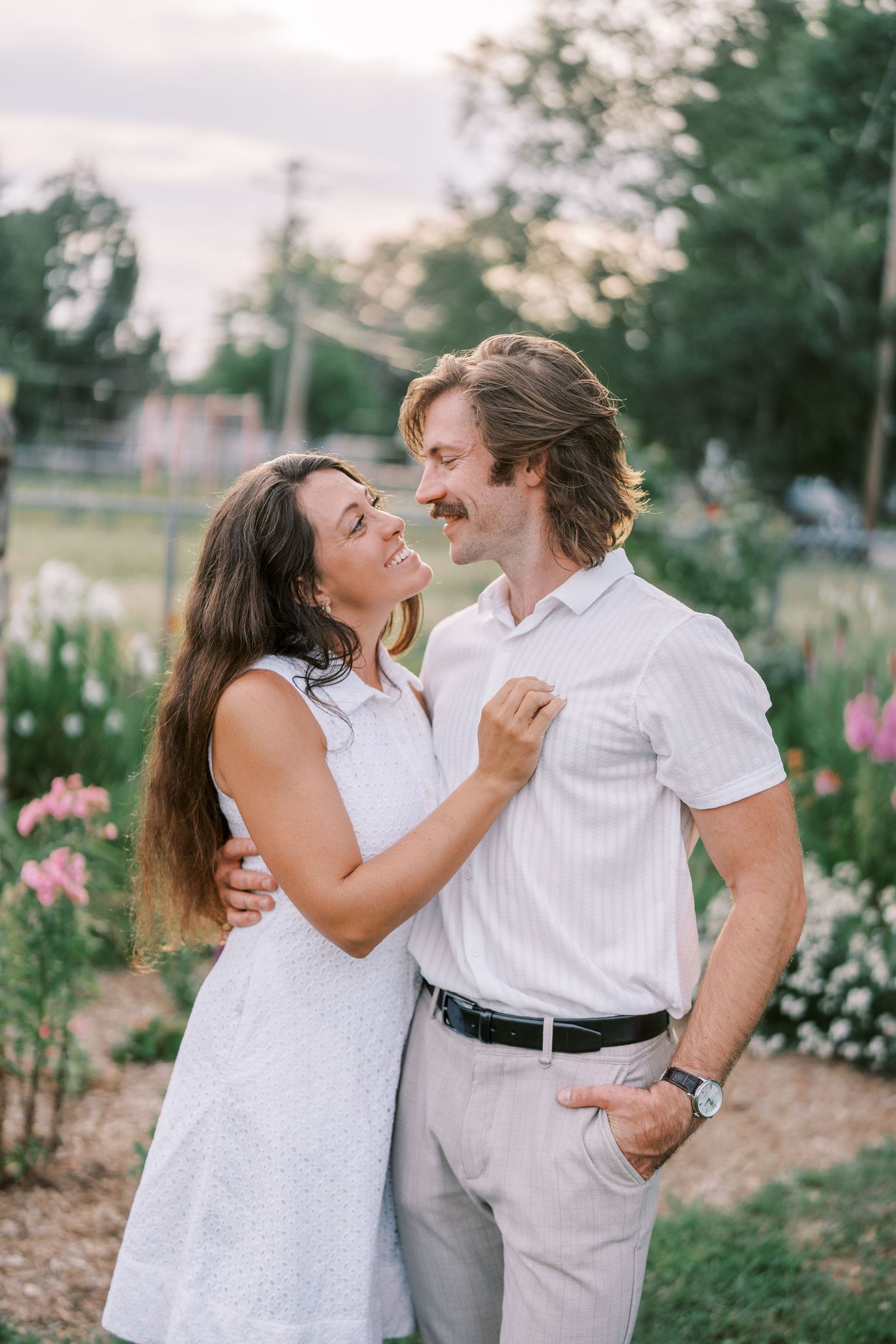 Joyful couple sharing laughs in a summer garden with blooming flowers.
