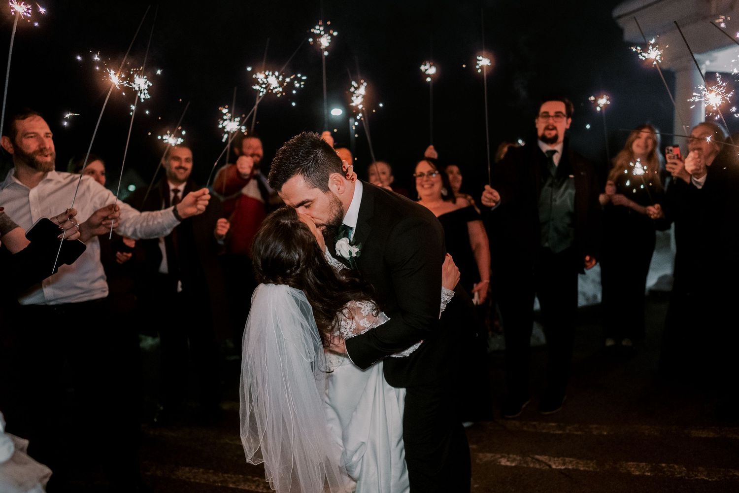 Wedding guests holding sparklers create a magical nighttime send-off tunnel for the celebration.