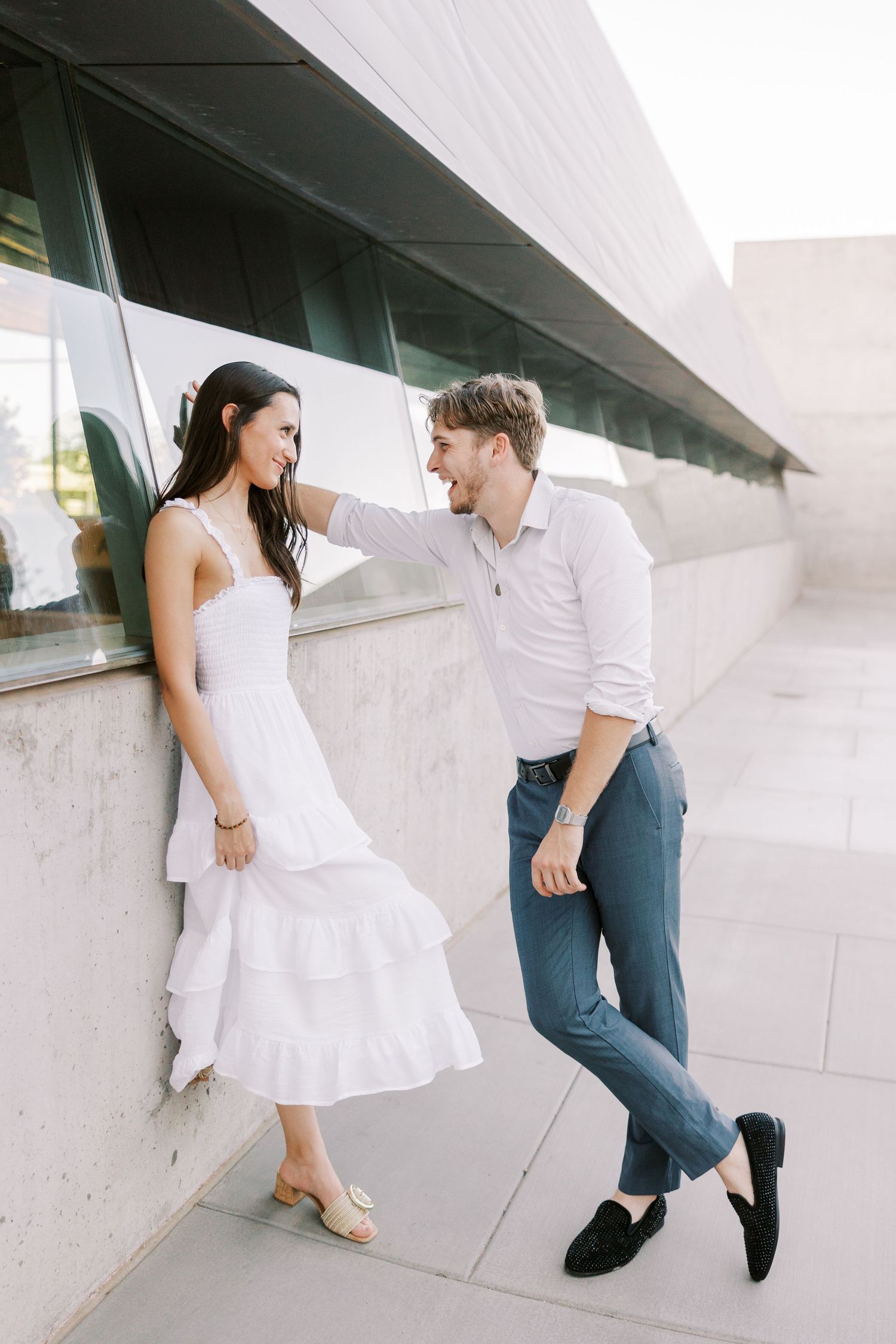 Couple in white and blue outfits posing playfully against a modern white architectural backdrop.