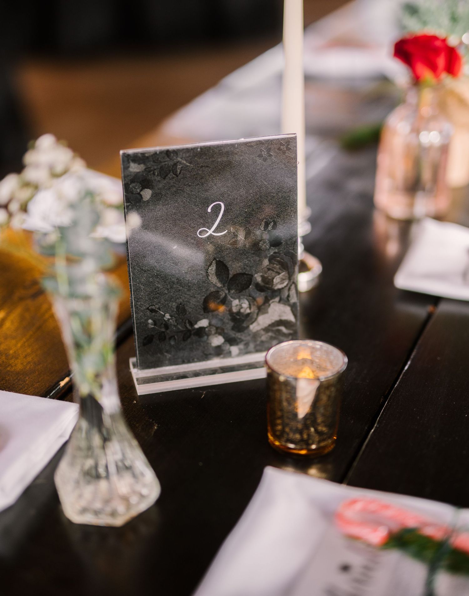 Elegant table number two displayed in grey acrylic stand with candlelight and floral arrangements in the background.